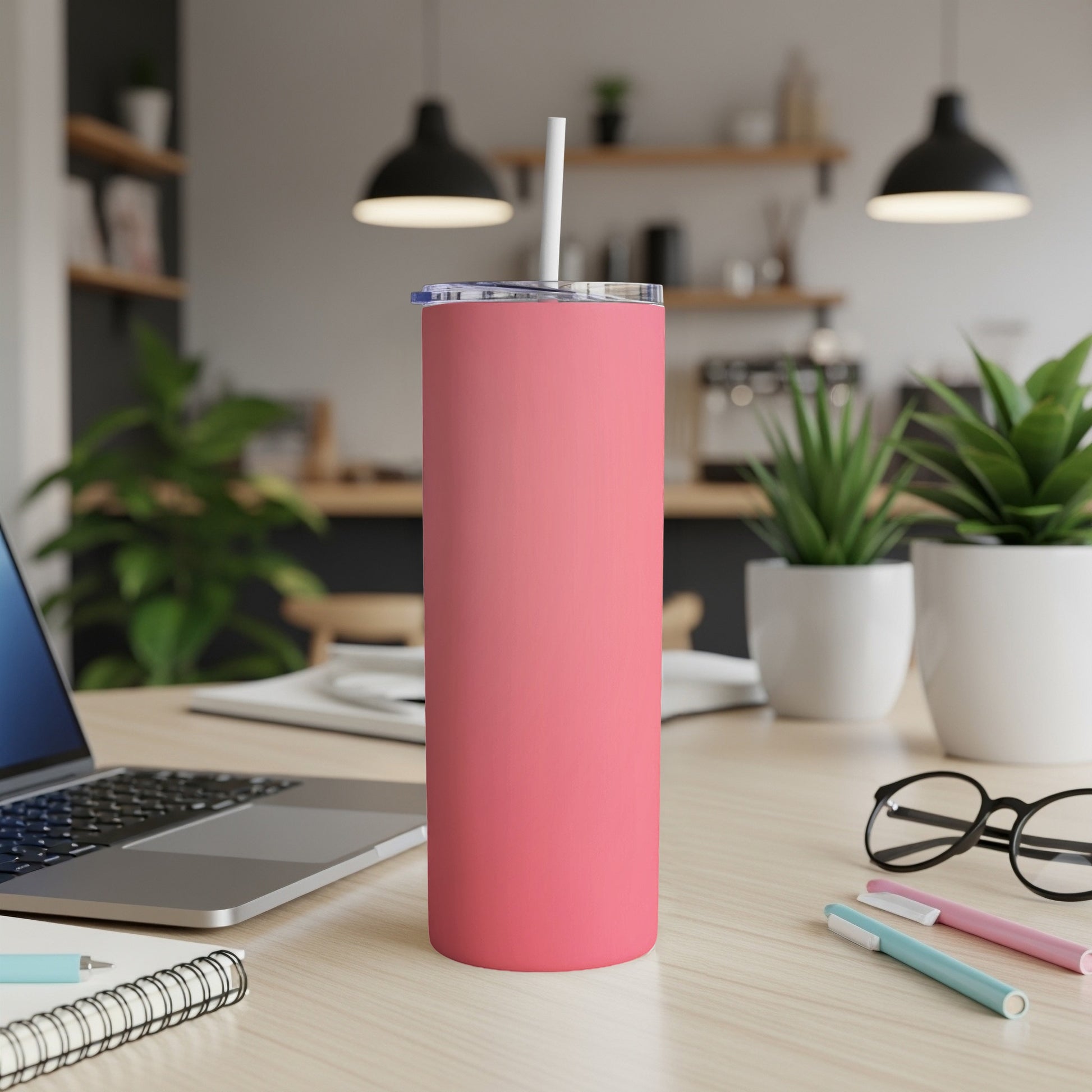 Pink skinny tumbler with straw on a desk next to a laptop.