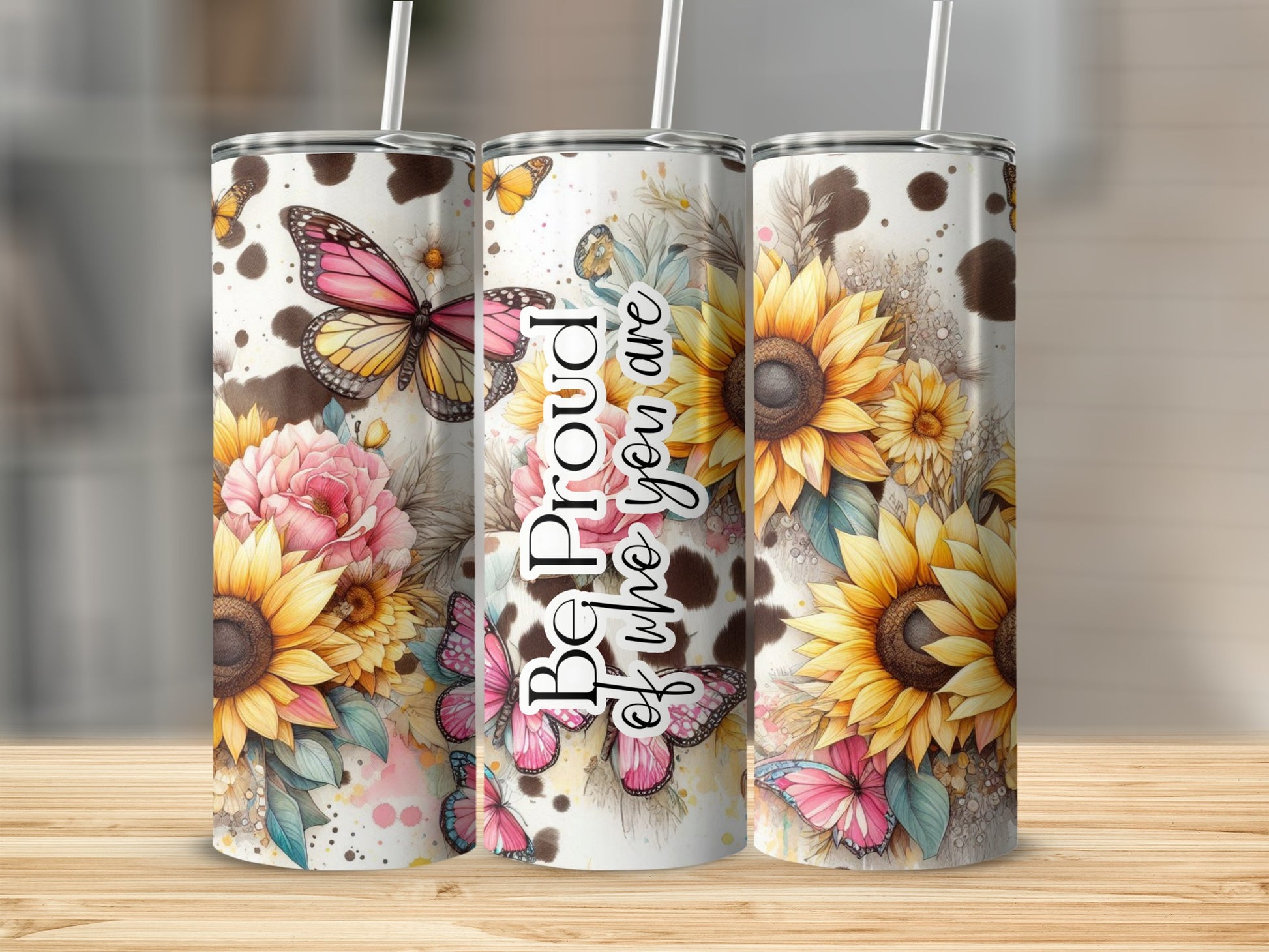 Three tumblers with sunflowers, butterflies, and cow print on a wooden surface.