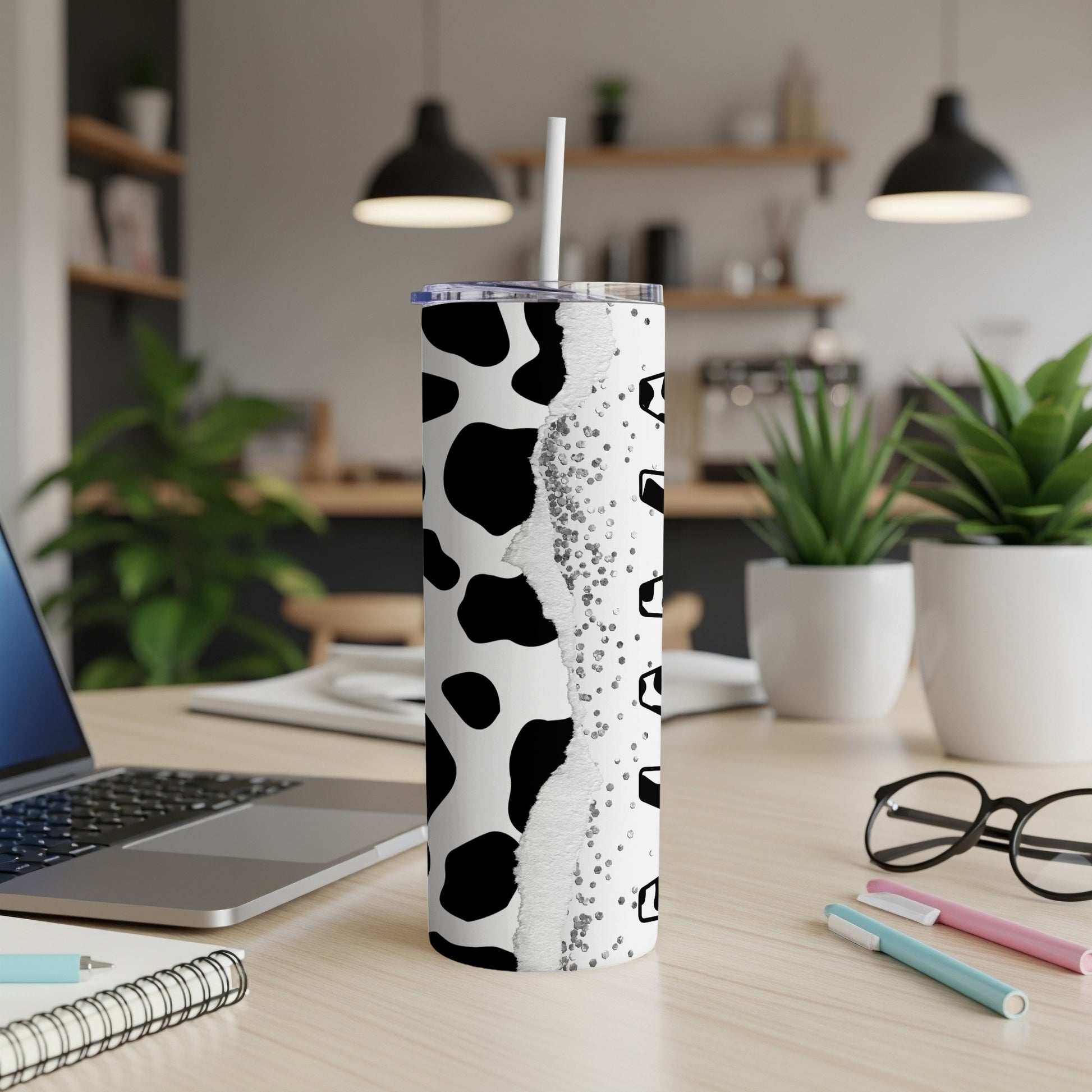 Cow print tumbler with a straw on a desk next to a laptop.