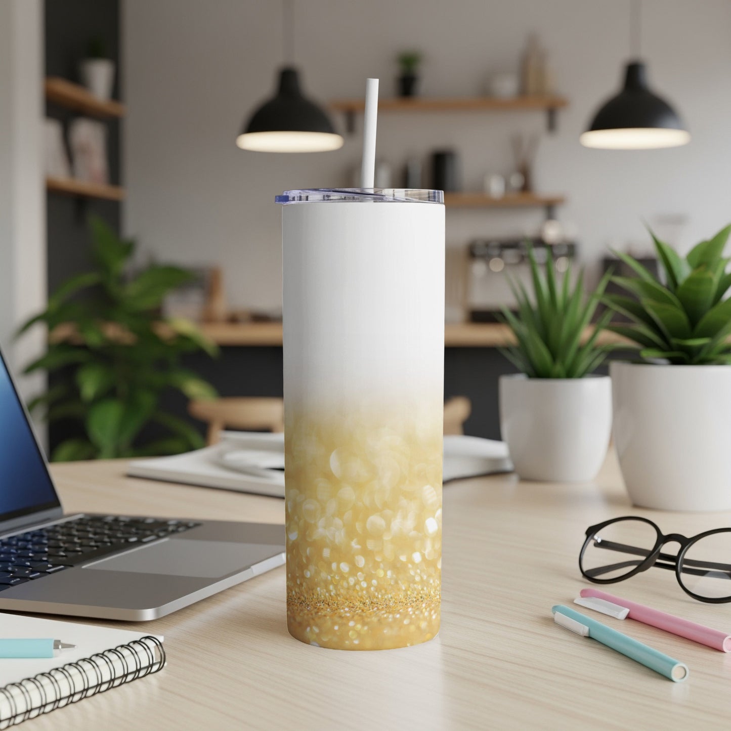 White and gold glitter tumbler with straw on a desk.