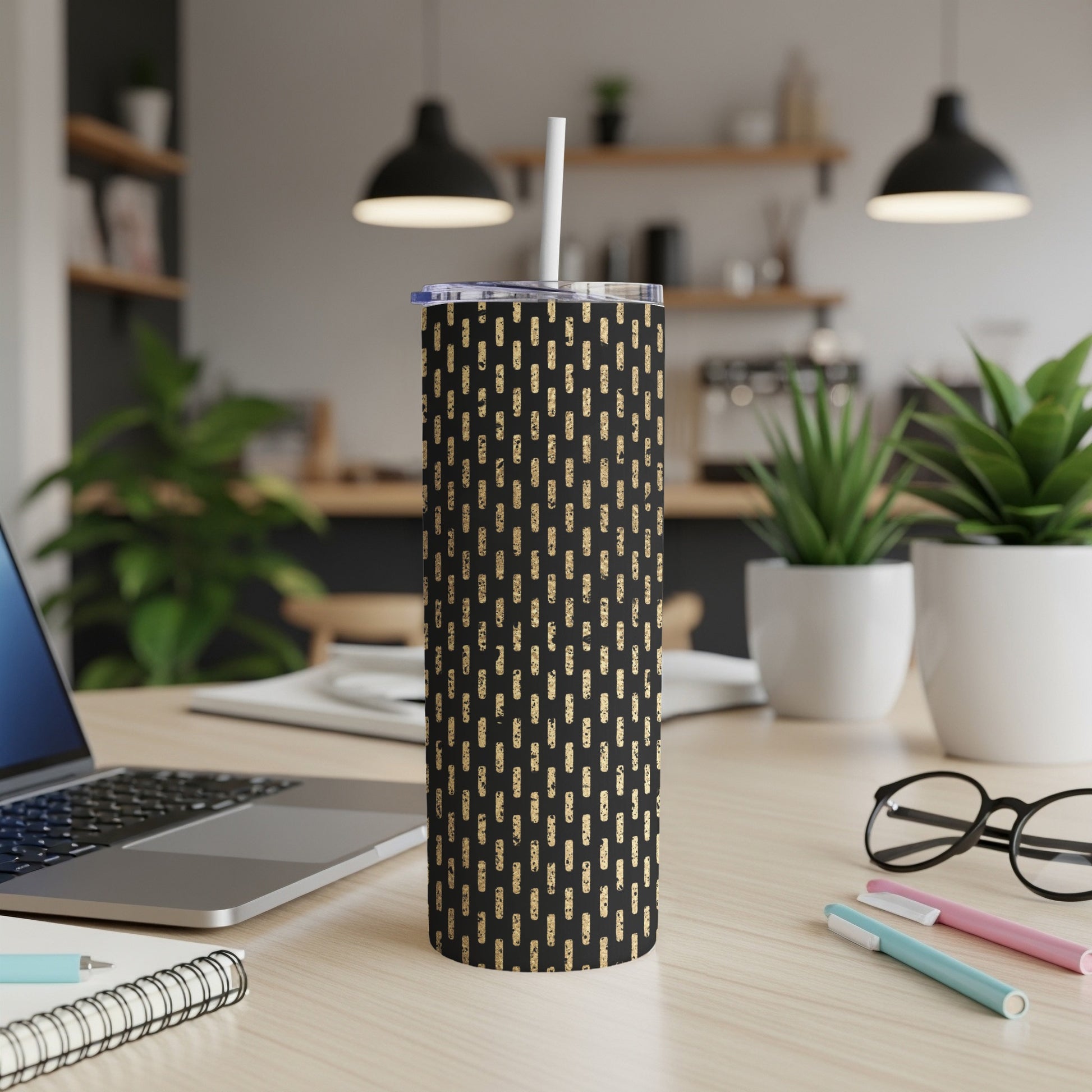 Black tumbler with gold dash pattern and straw on a desk.