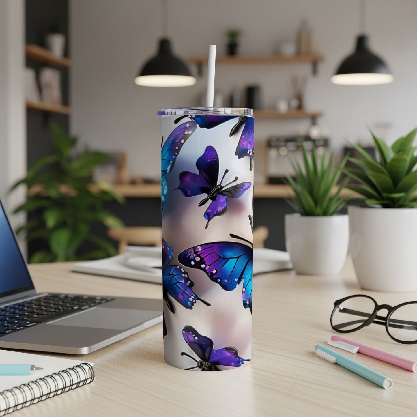 Tumbler with purple and blue butterflies, on a desk with a laptop.
