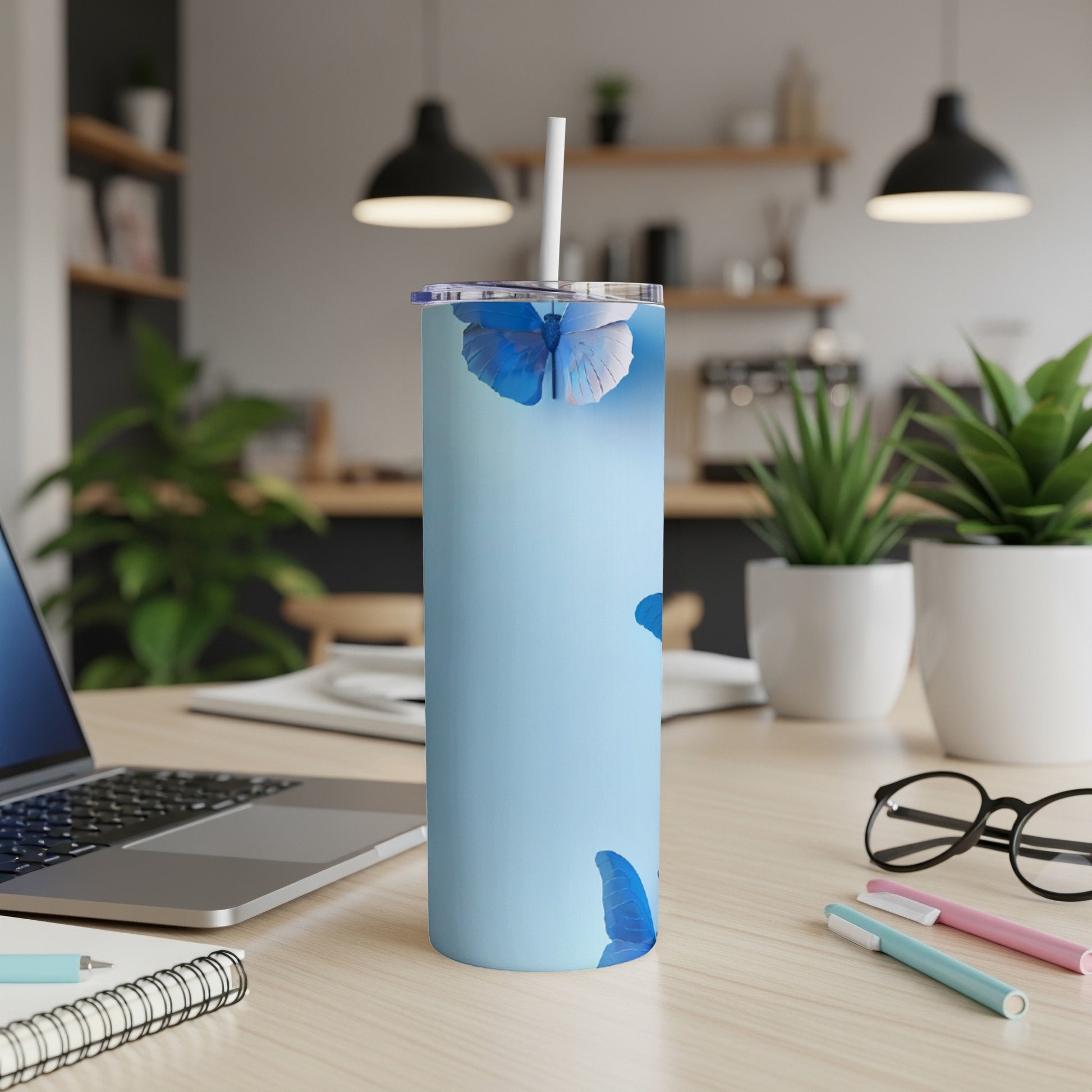 Light blue tumbler with blue butterflies and a straw on a desk.