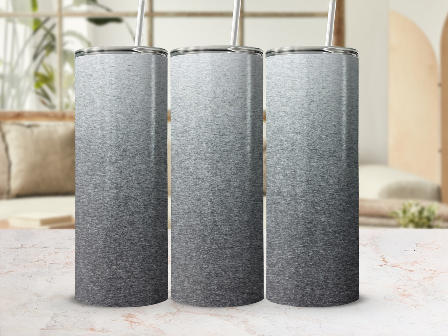 Three silver ombre tumblers with straws on a marbled surface.