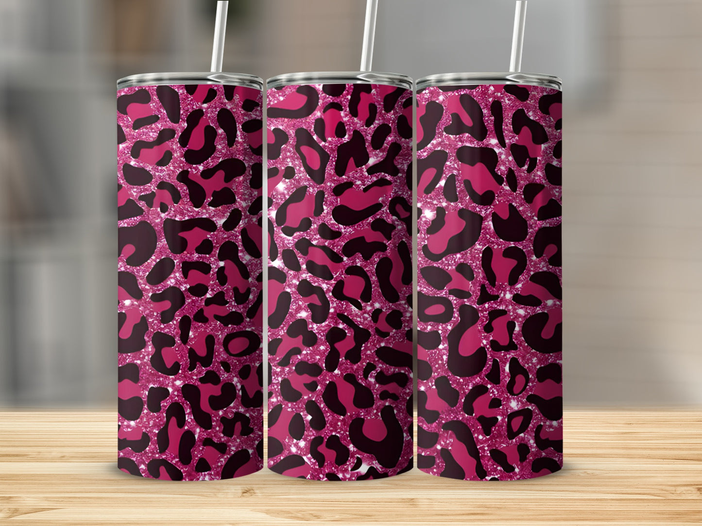 Three pink leopard print tumblers with straws on a wooden surface.