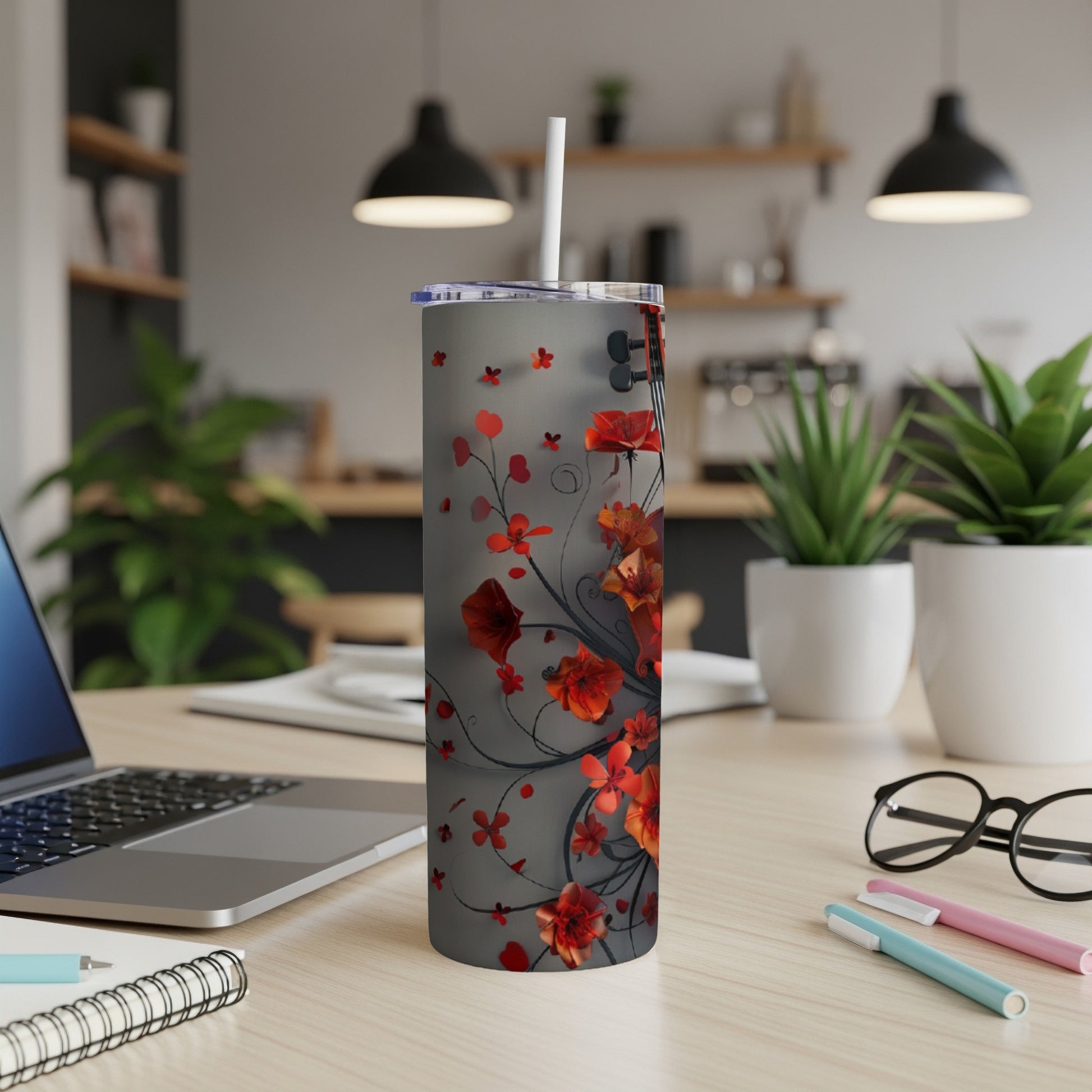 Gray tumbler with red floral design and white straw on a desk.