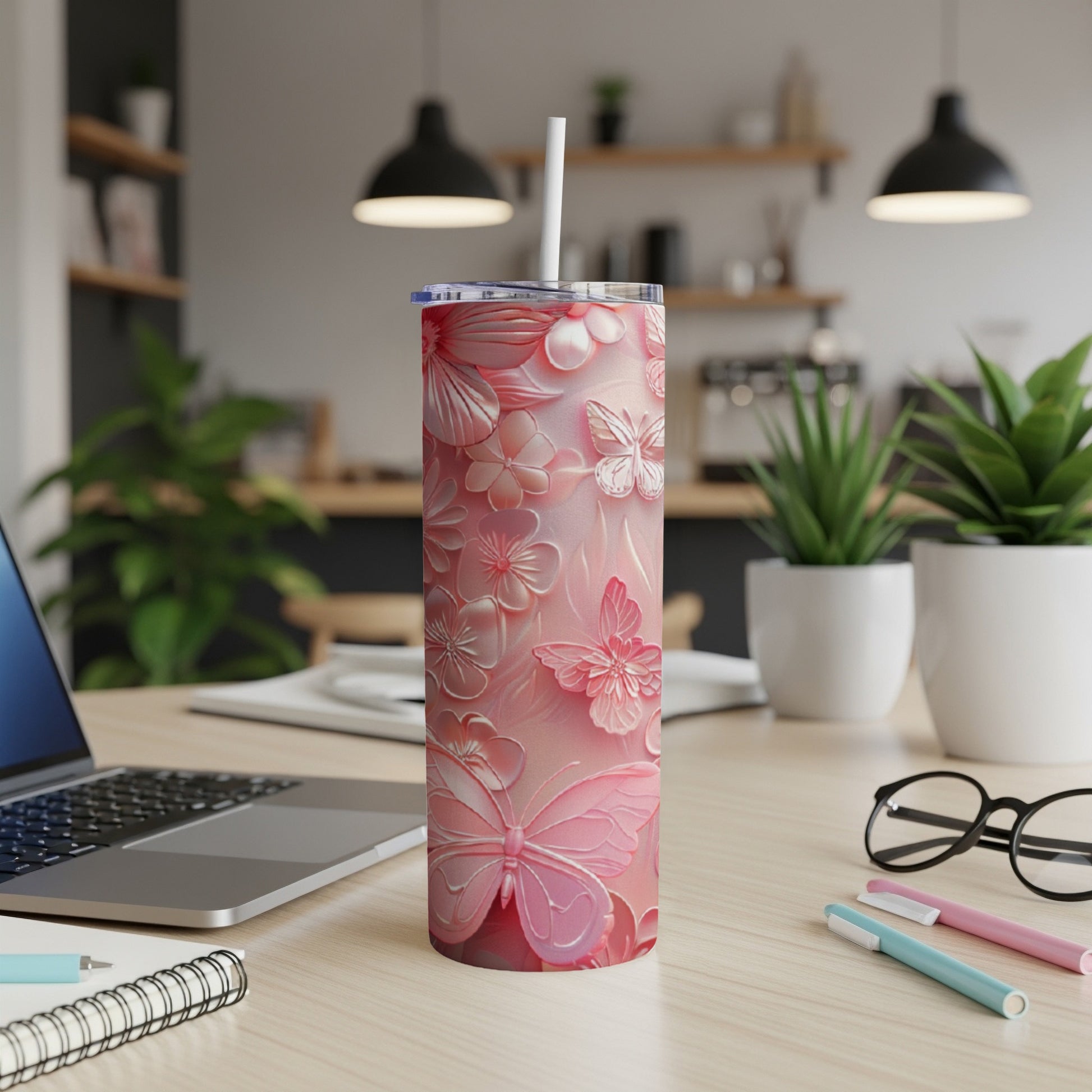 Pink floral and butterfly embossed tumbler with straw on a desk.
