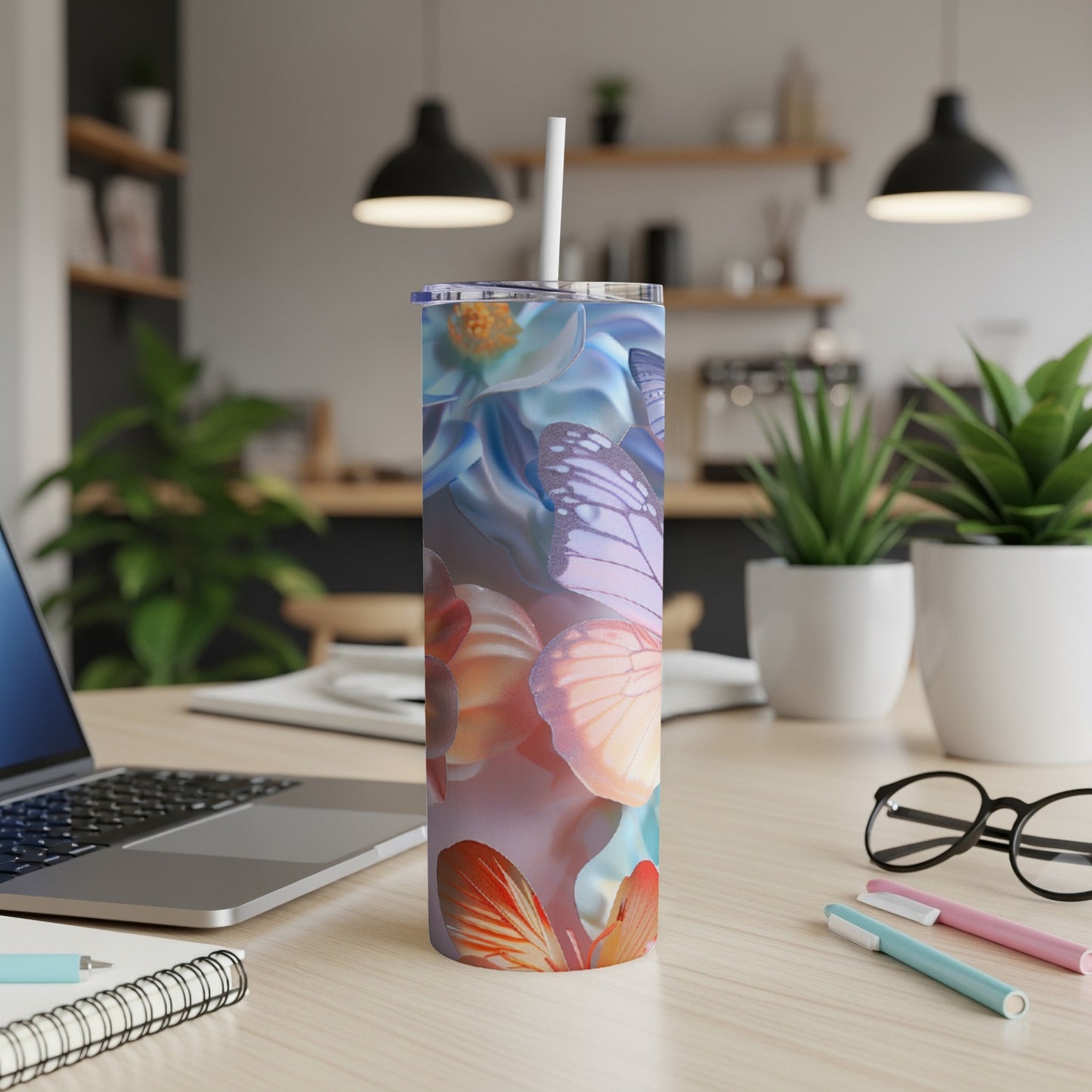Tumbler with floral and butterfly design on a wooden desk with laptop and pens.