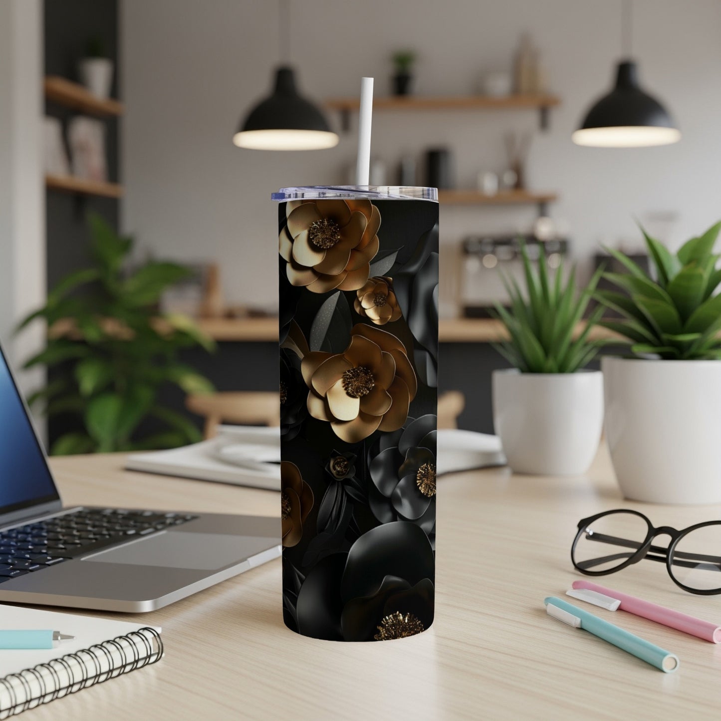 Black tumbler with gold floral design and white straw, on a desk.