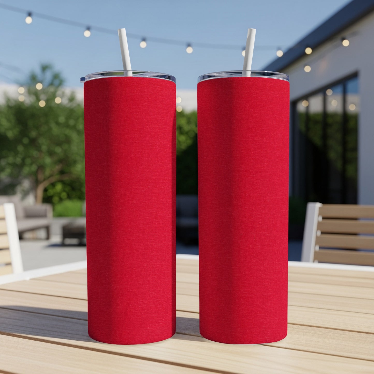 Two red tumblers with straws on a wooden table outdoors.