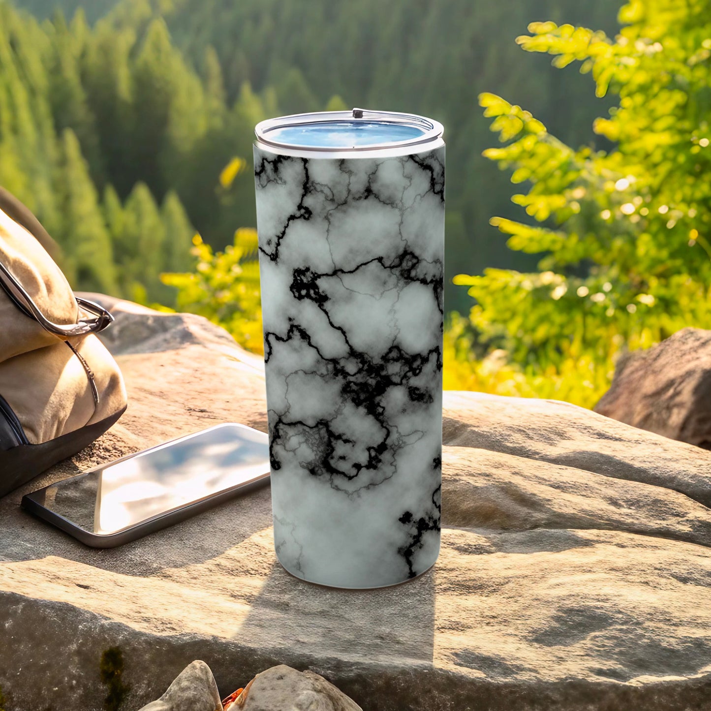 Tumbler with black and white marble pattern on a rock with a phone and backpack.