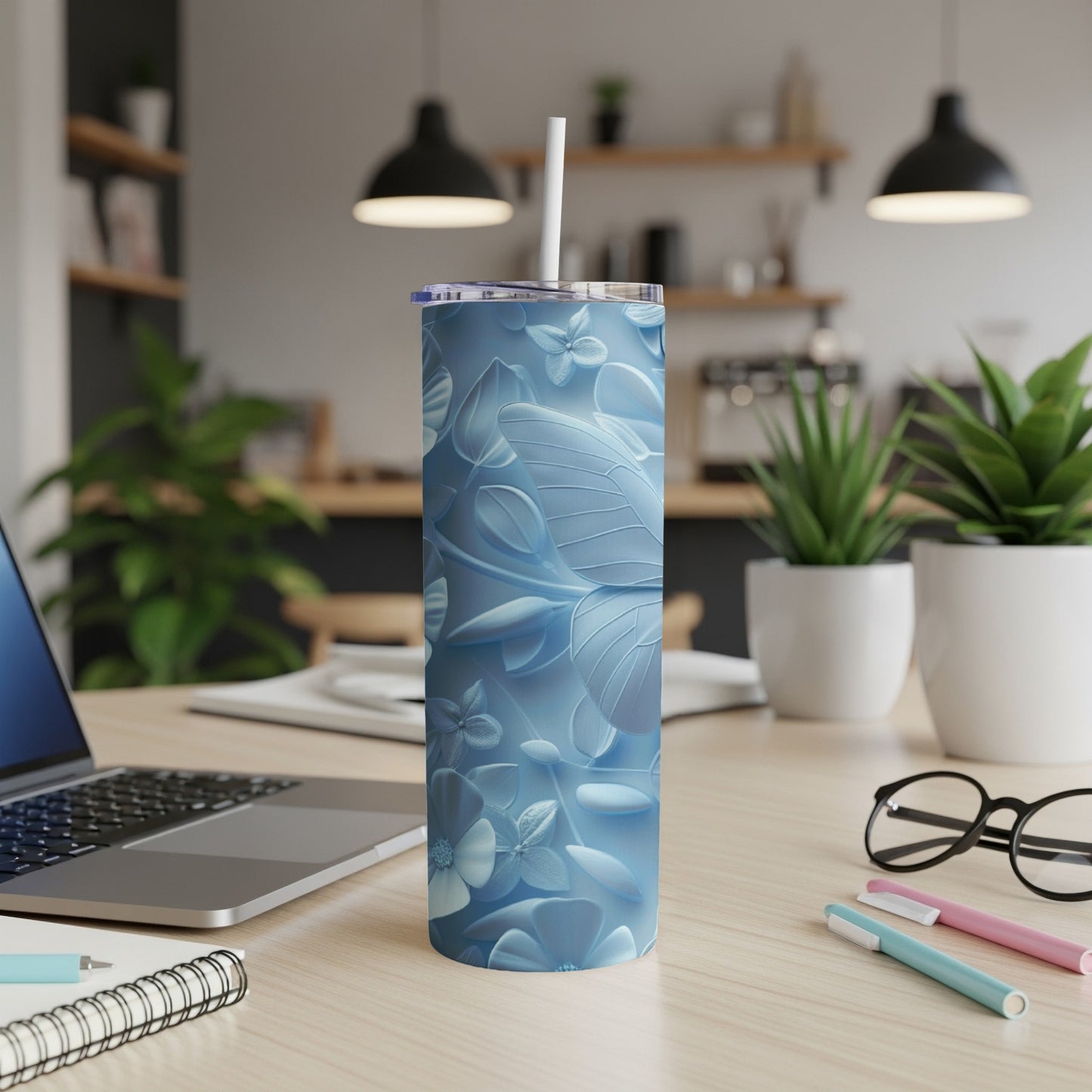 Blue floral tumbler with straw on a desk with a laptop and pens.
