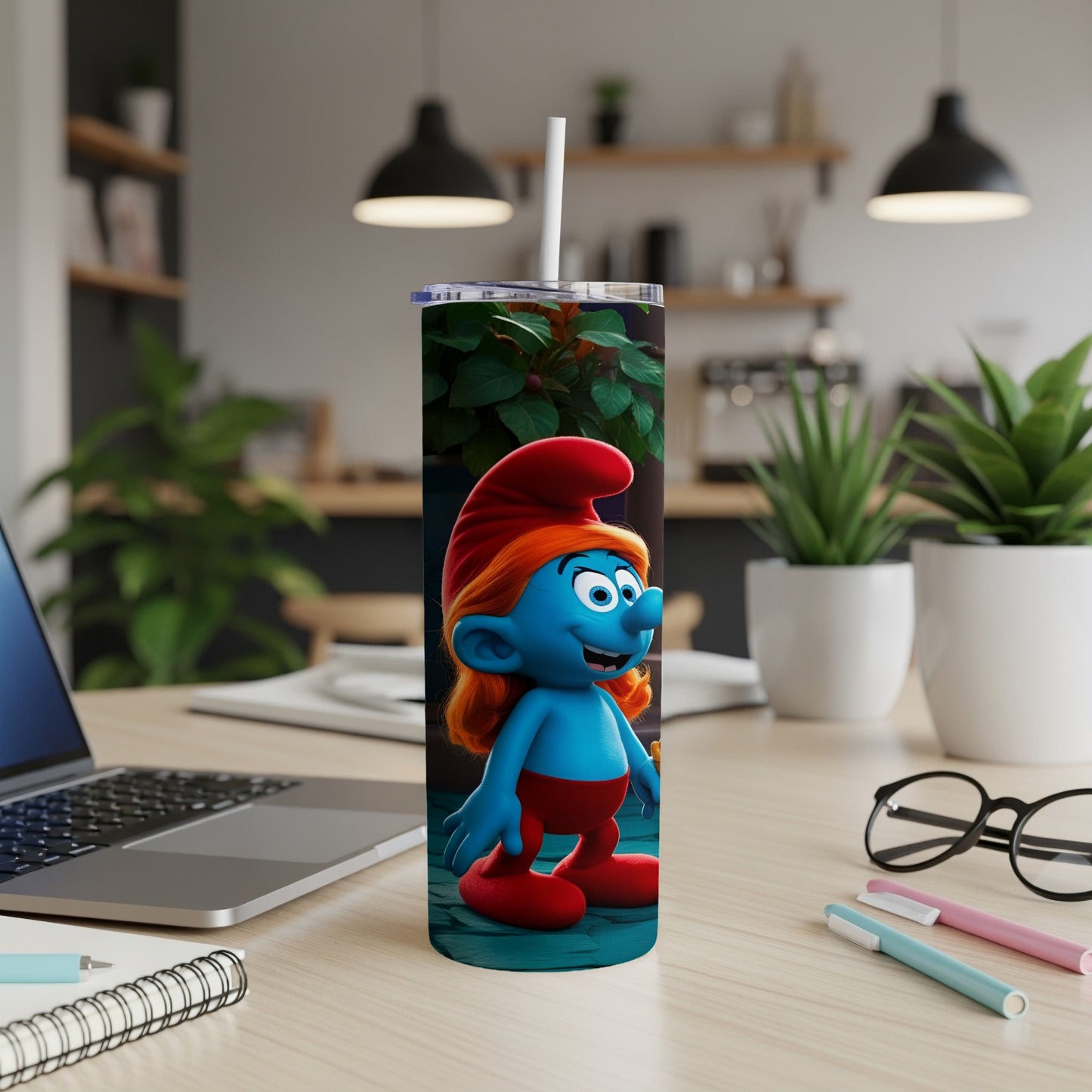 Smurf character in red hat on a blue tumbler with straw, on a desk.