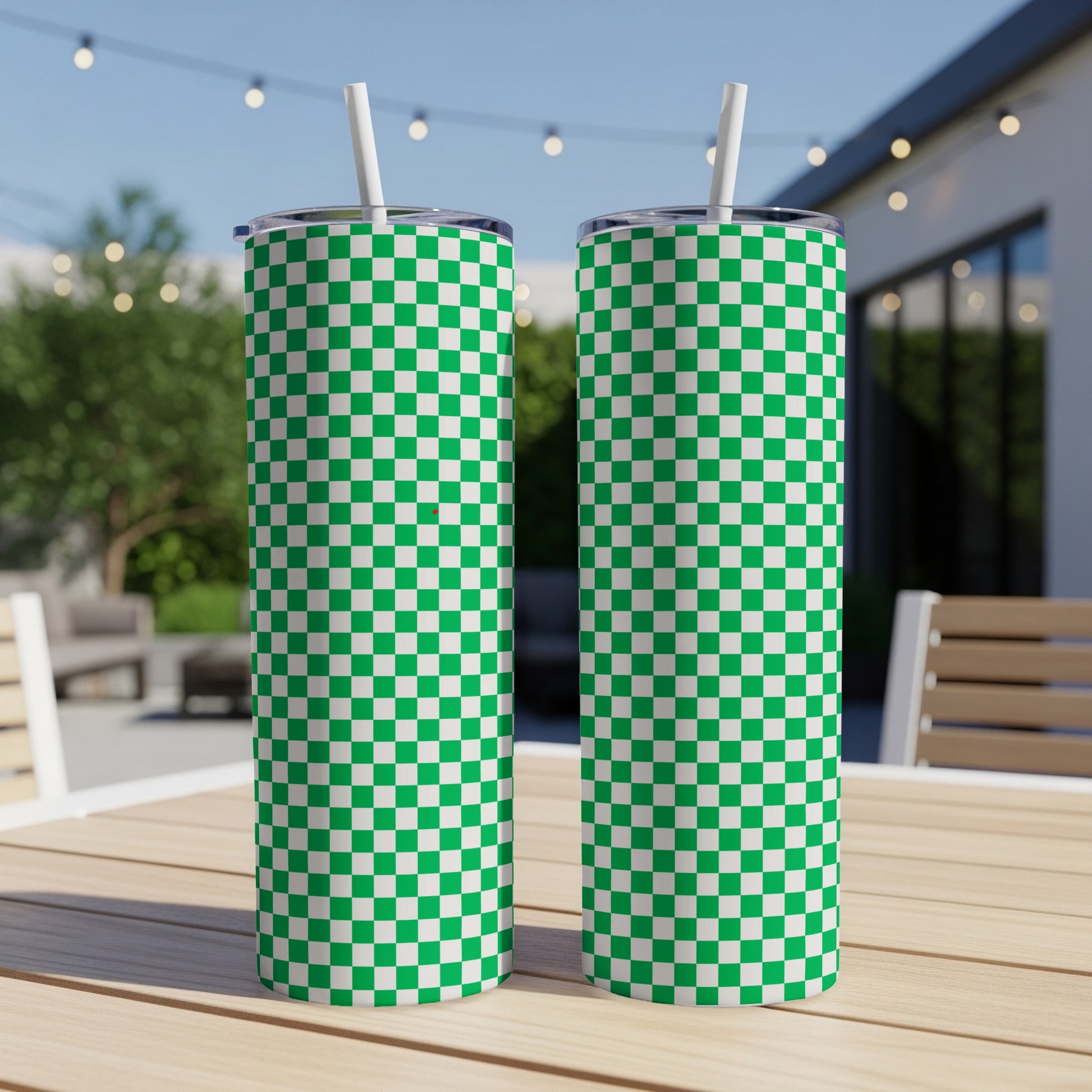 Two green and white checkered tumblers with straws on a wooden table.
