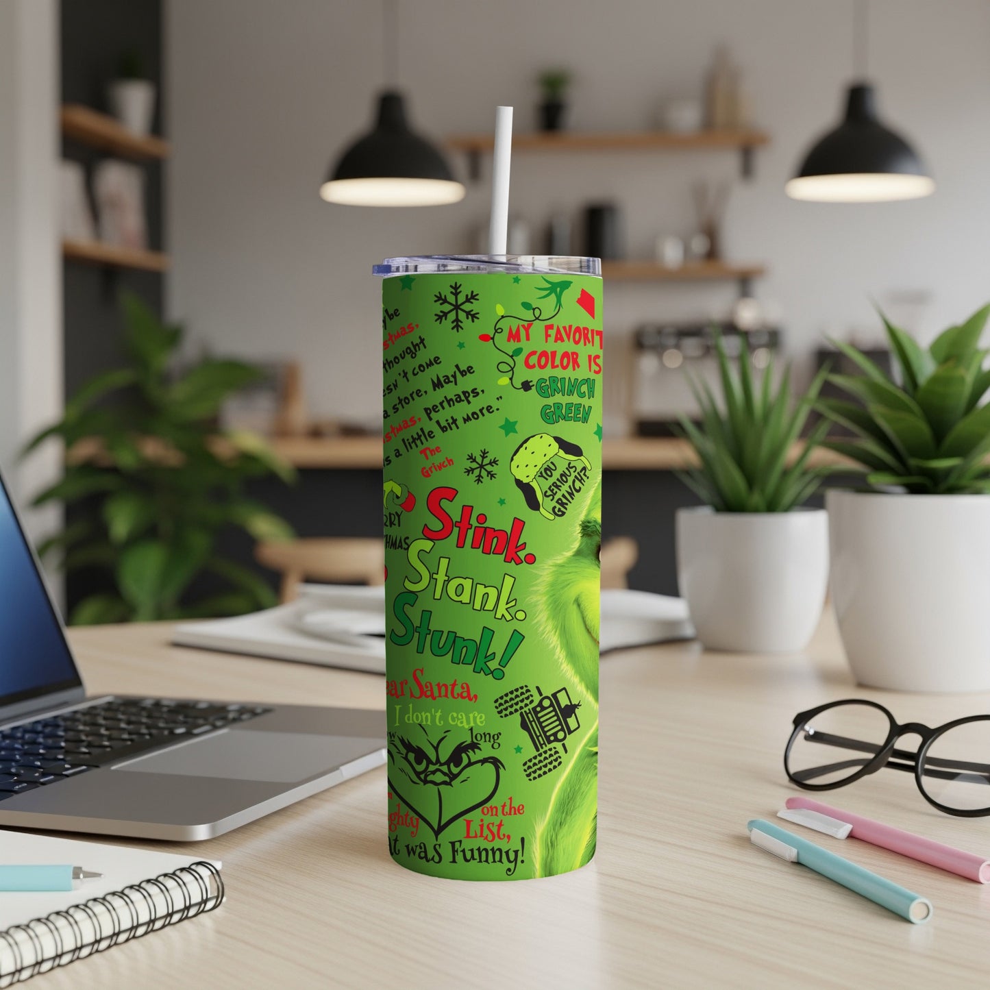 Green Grinch tumbler with quote "Stink. Stank. Stunk!" on a desk.
