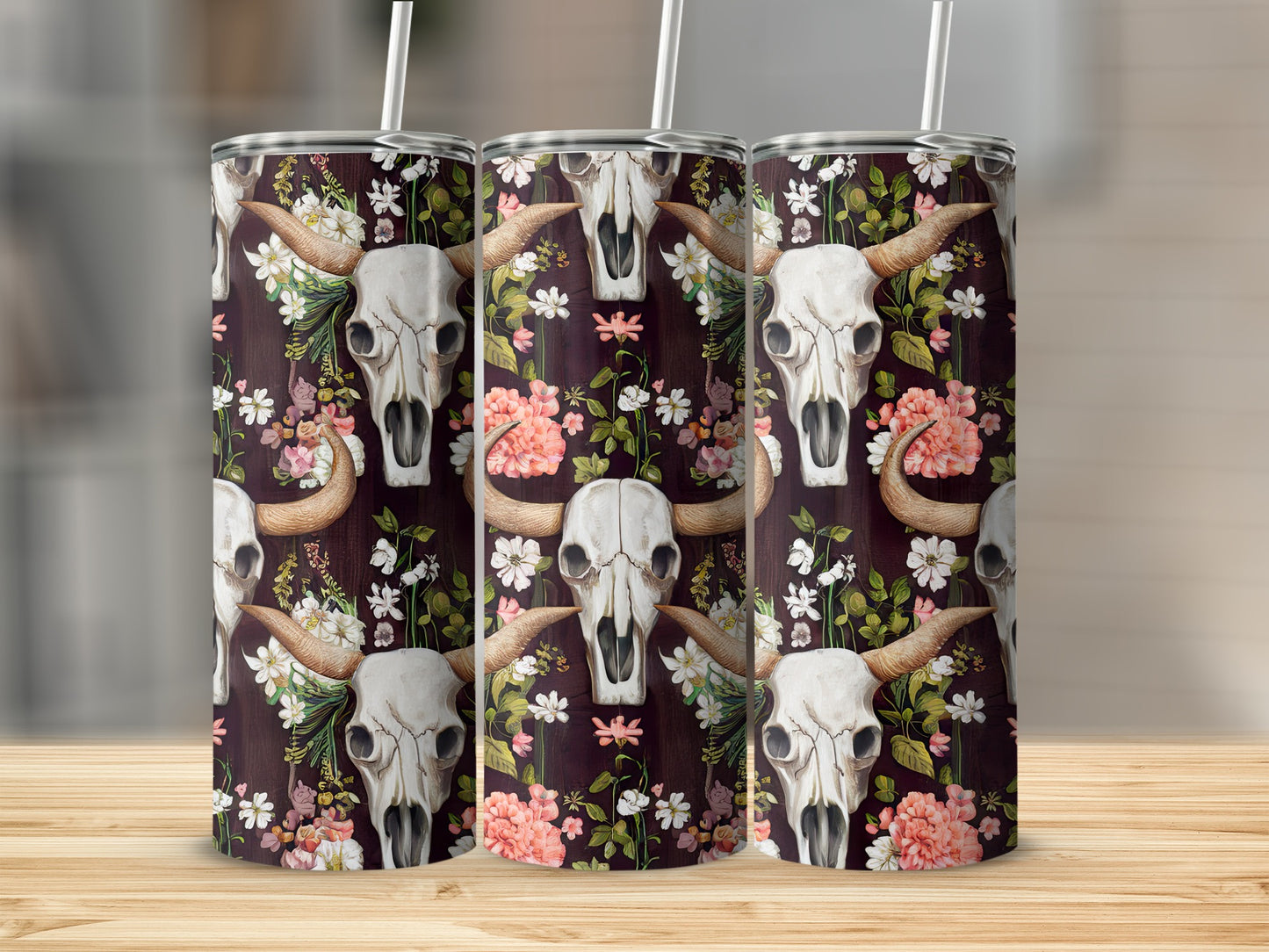 Floral skull pattern on three metal tumblers with straws on a wooden surface.