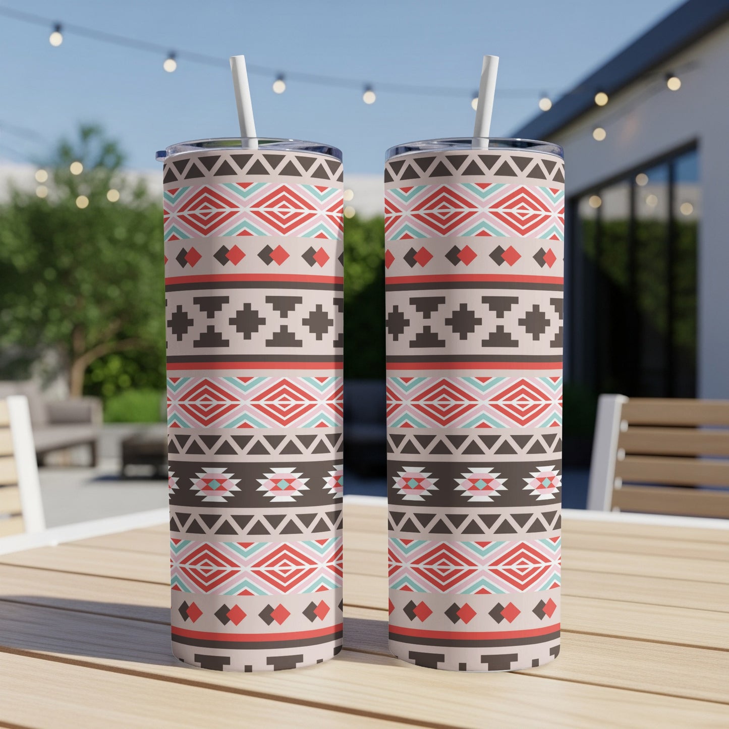 Two tumblers with a southwestern geometric pattern and white straws on a wooden table.