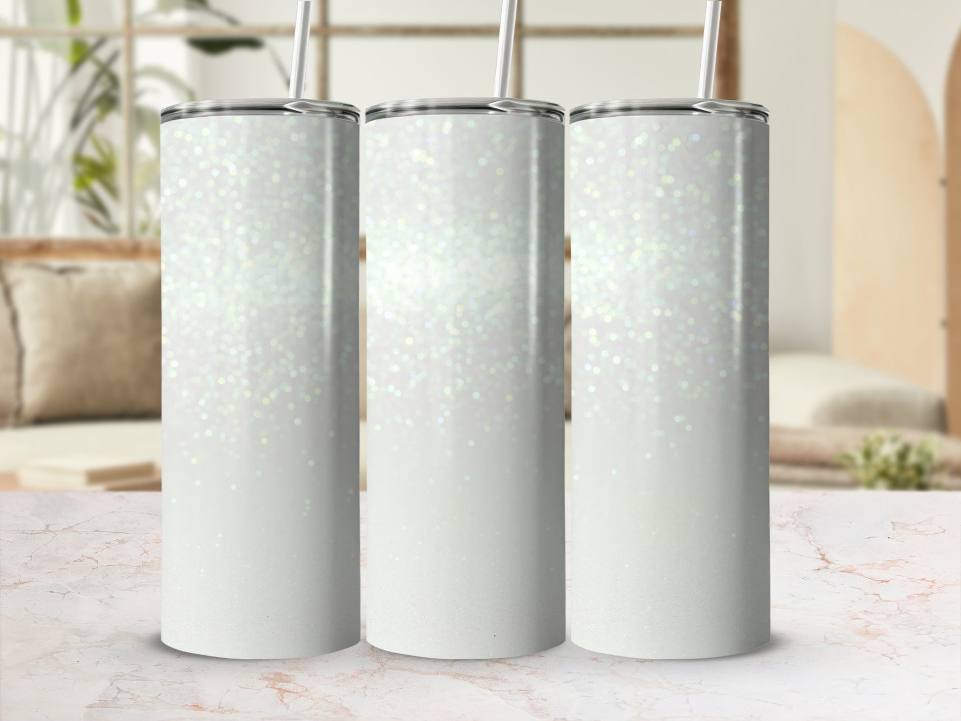 Three white glitter tumblers with straws on a marble surface.