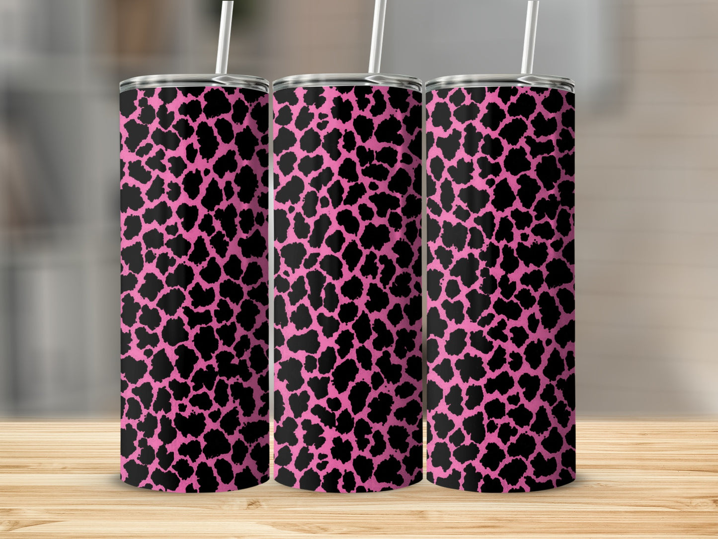 Three tumblers with a pink and black leopard spot design stand on a wooden surface.