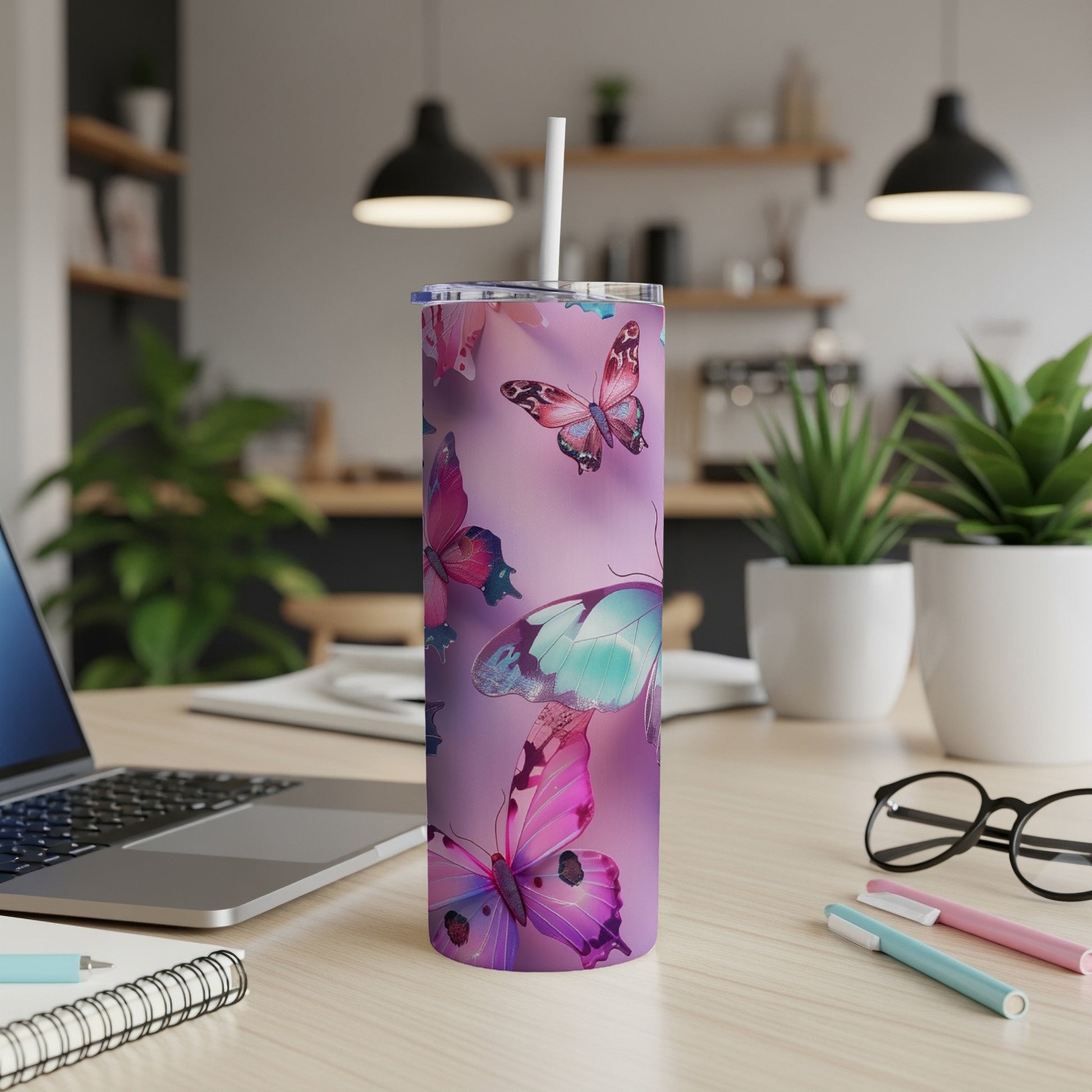 Purple tumbler with colorful butterflies, straw, laptop, and pens on a desk.