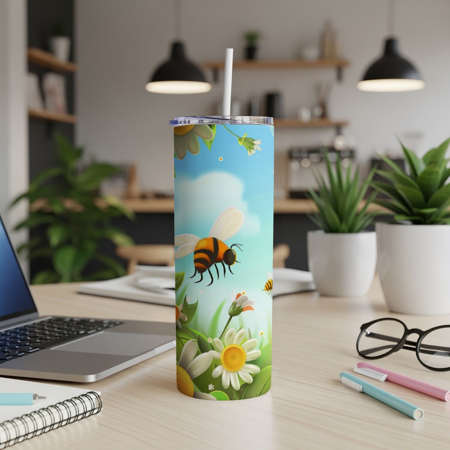 Tall tumbler with bees and flowers, resting on a desk next to a laptop.