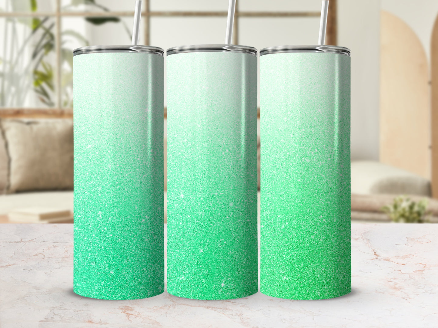 Three teal and green glitter tumblers with straws on a marble surface.