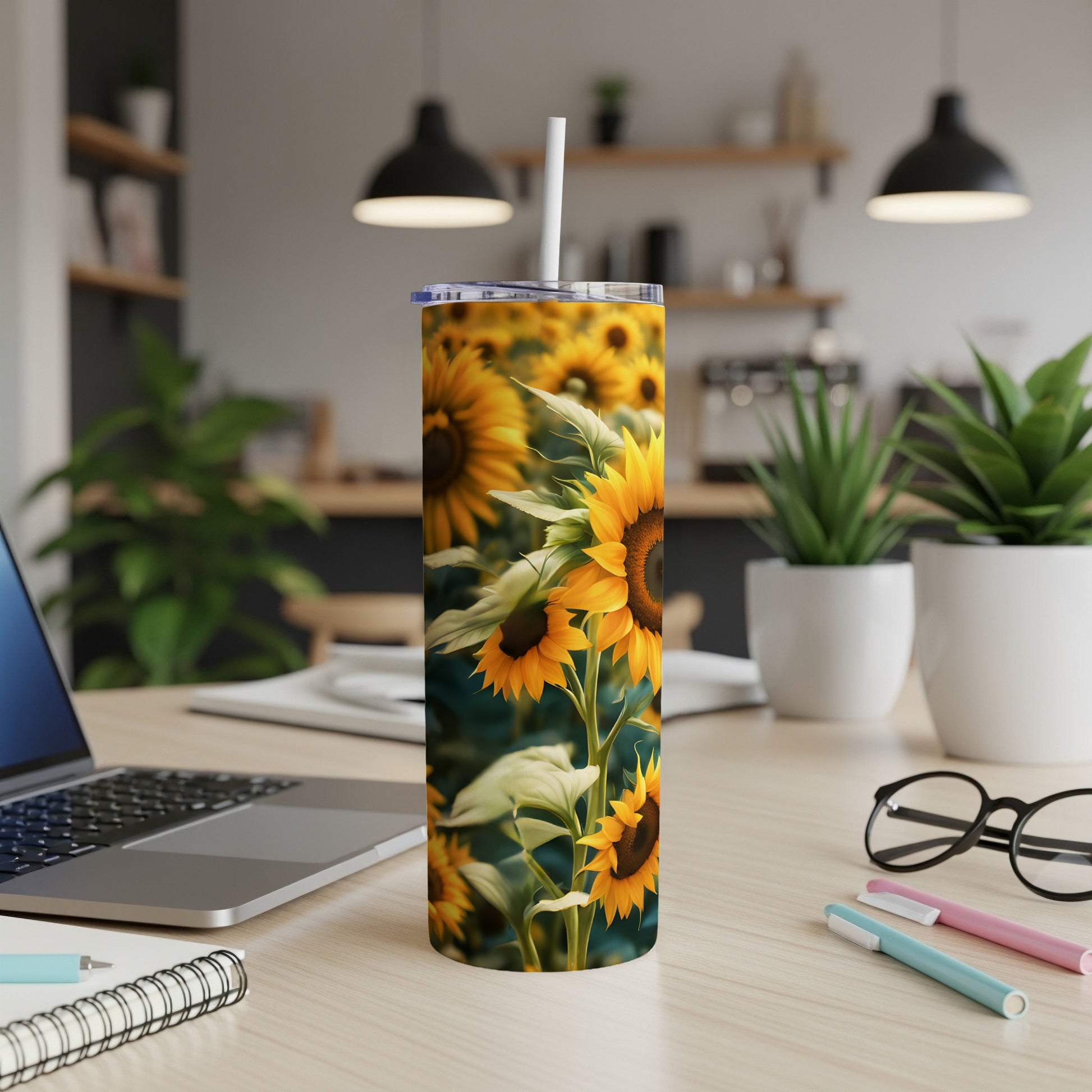 Sunflower tumbler with a white straw on a desk with a laptop and pens.