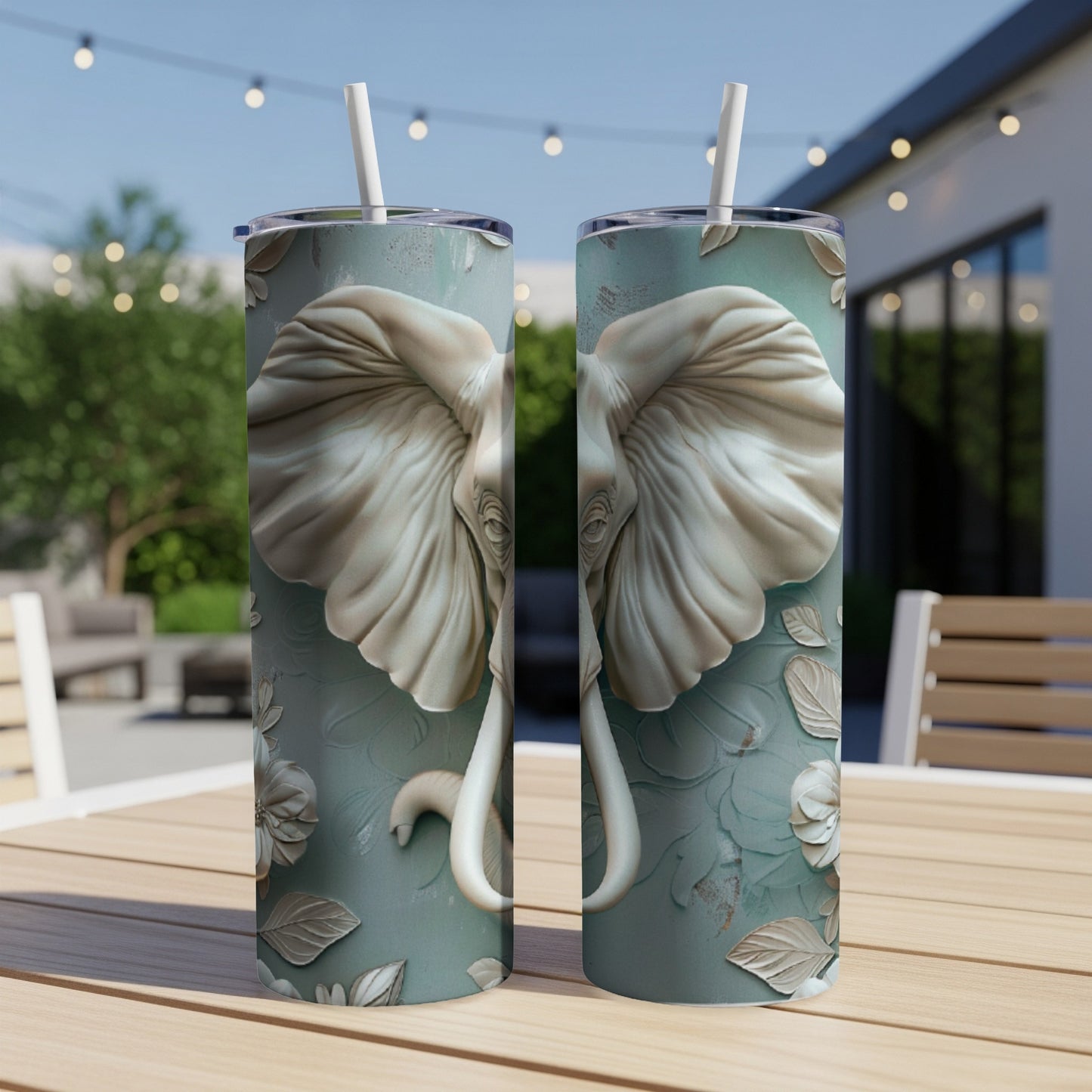Two tumblers with elephant faces and floral designs sit on a wooden table outdoors.