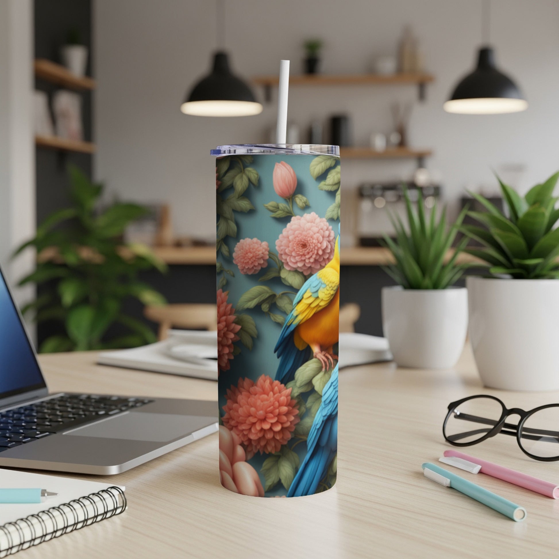 Floral tumbler with two parrots on a desk with a laptop.