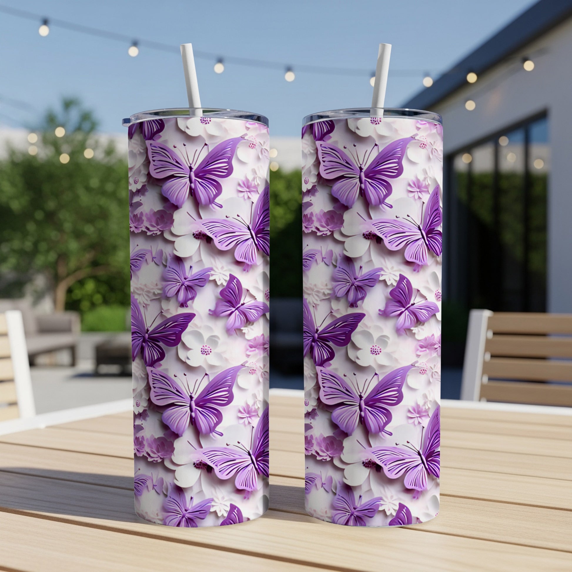 Two purple butterfly and flower patterned tumblers with straws on a table.