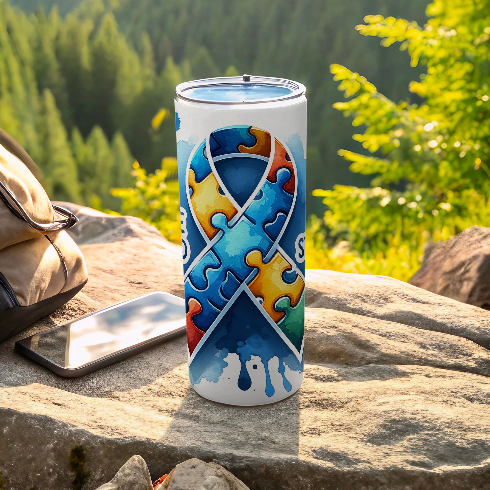 Blue autism awareness ribbon tumbler with puzzle pieces, outdoors.