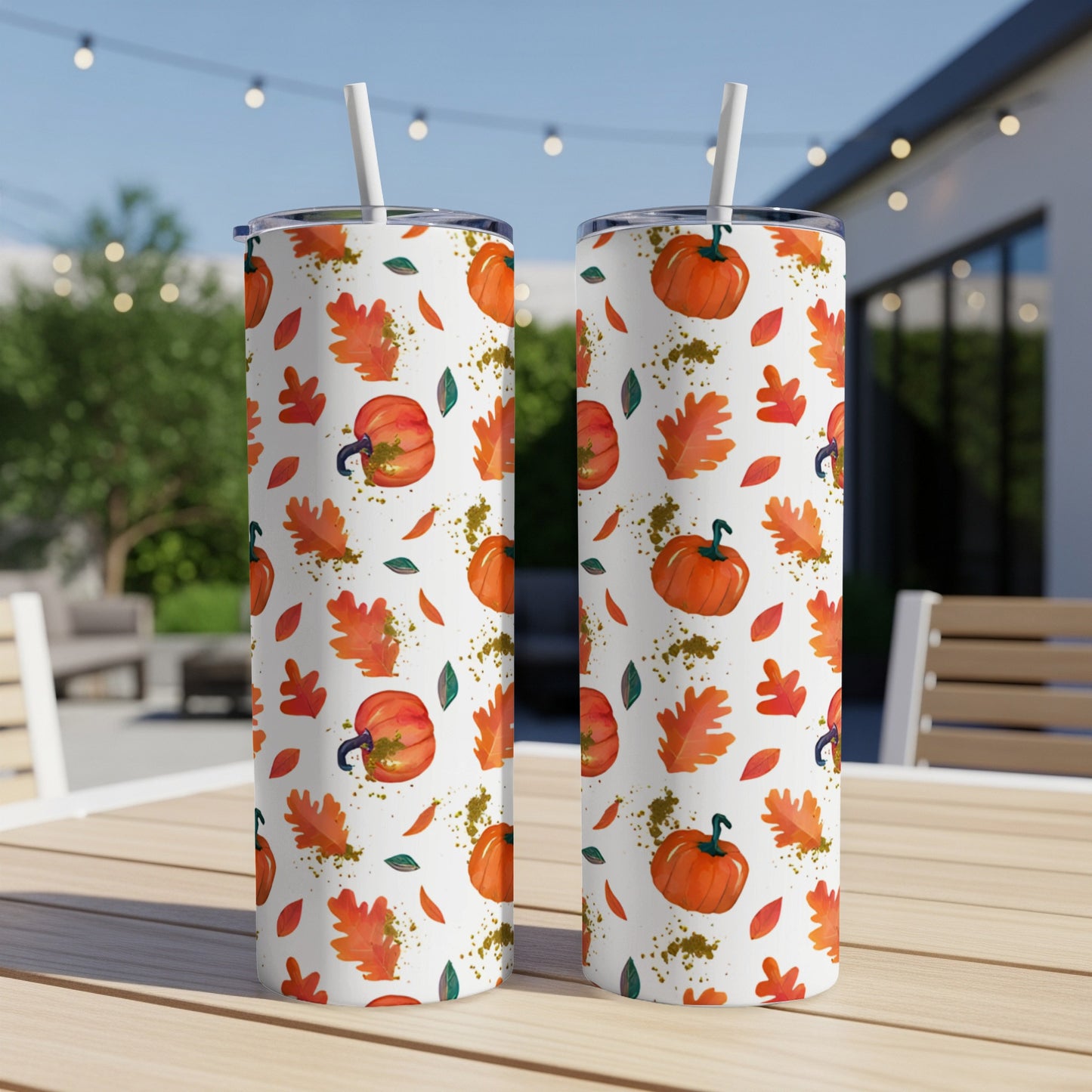 Two white tumblers with a pumpkin and fall leaf pattern on a table.