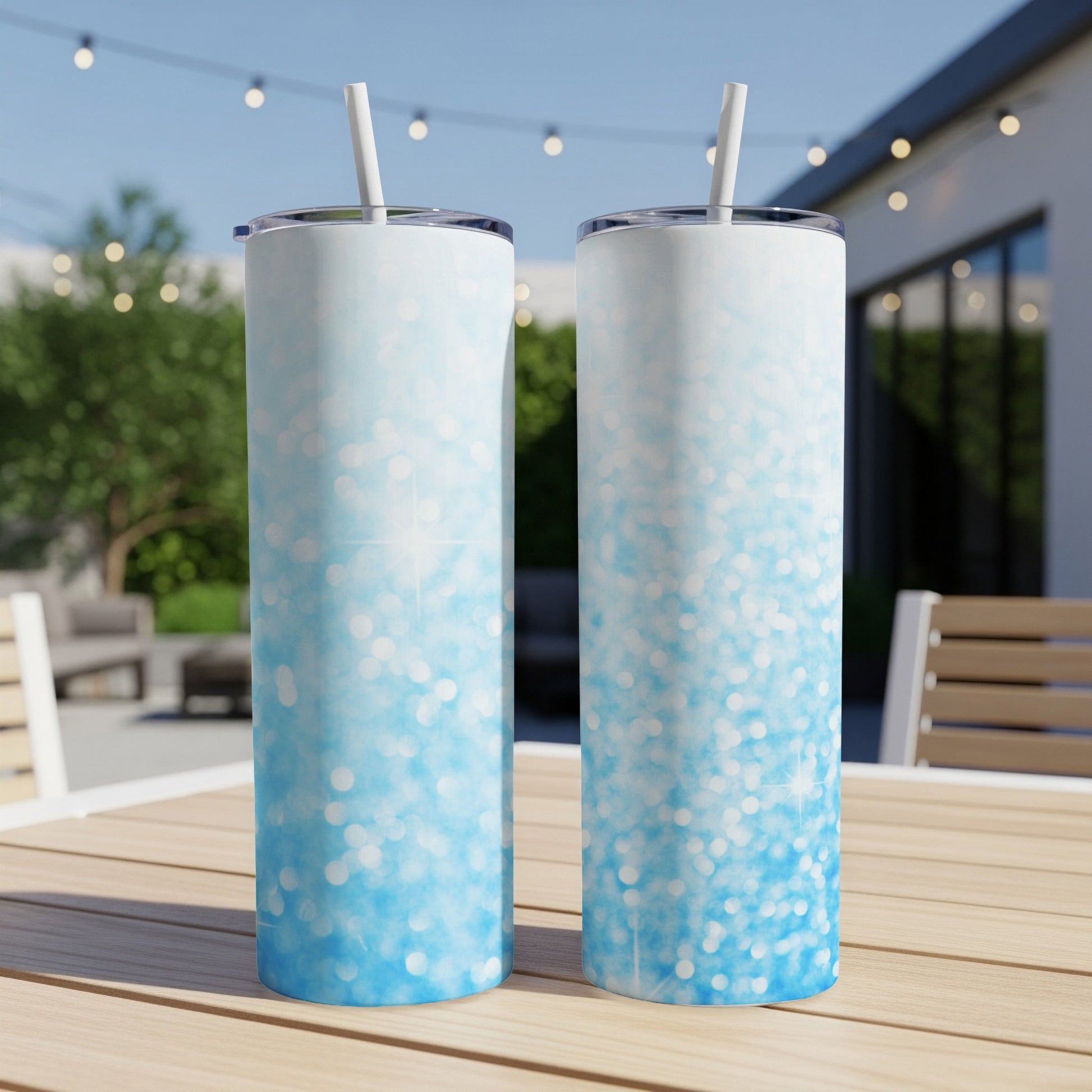 Two blue glitter gradient tumblers with straws on a wooden table outdoors.