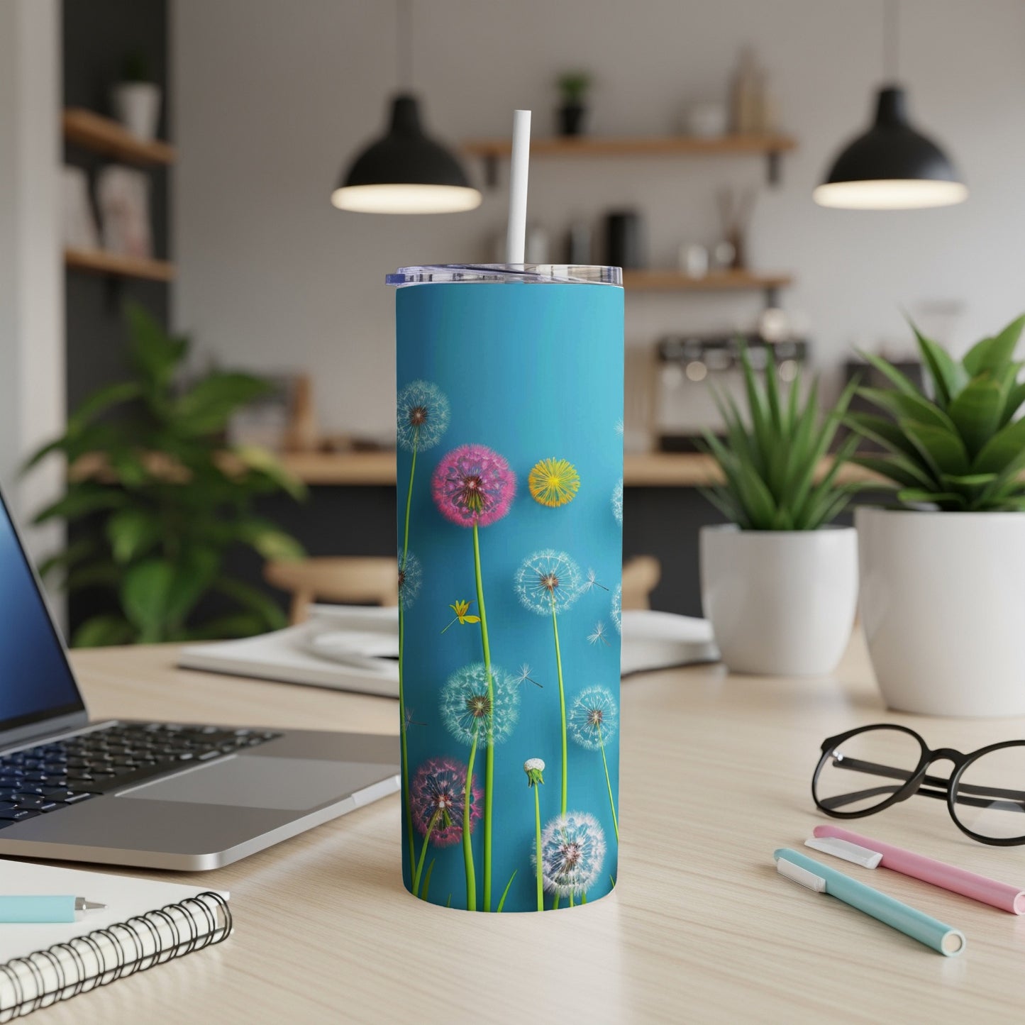 Blue tumbler with dandelions and seeds on a desk with a laptop.
