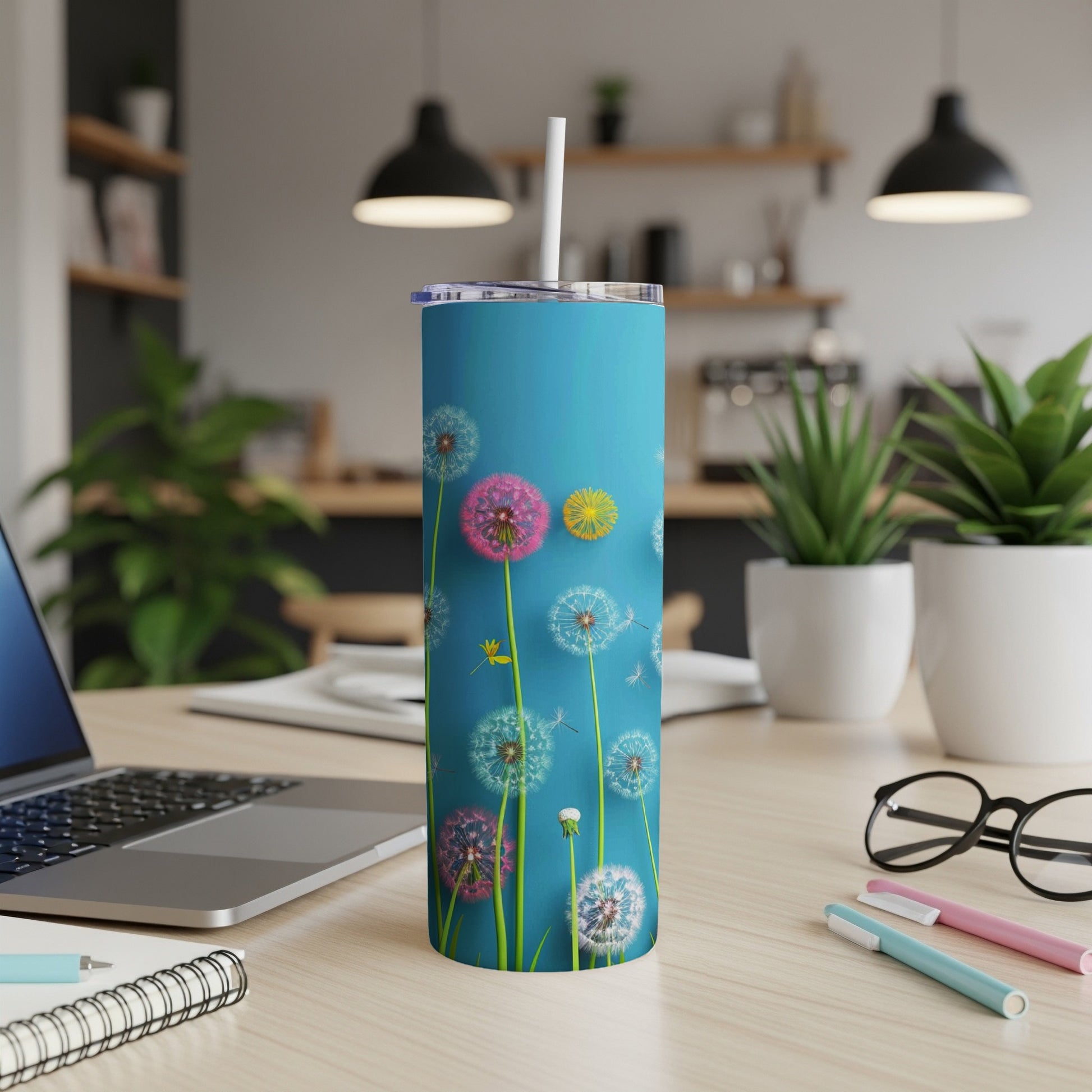 Blue tumbler with dandelions and seeds on a desk with a laptop.