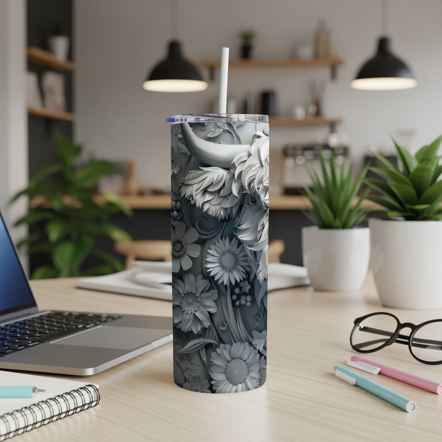 Gray sculpted tumbler with floral and animal designs on a desk.