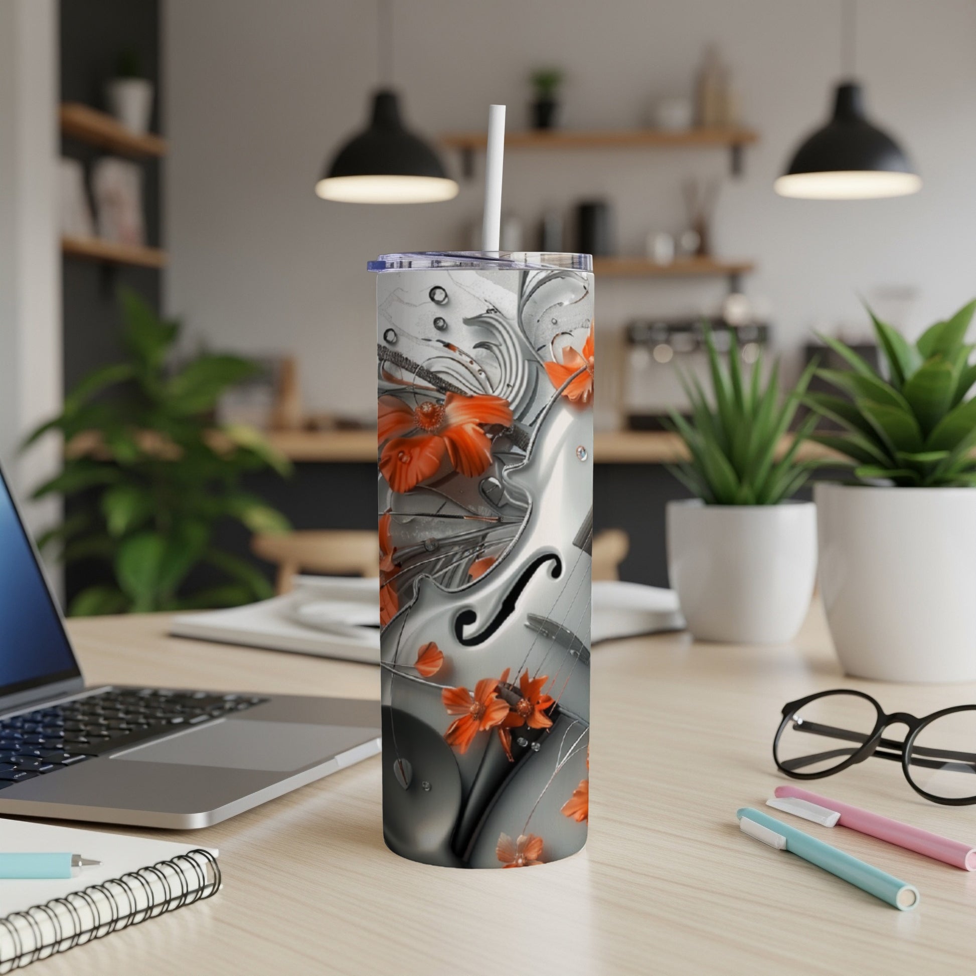Tall, silver tumbler with floral and violin designs, on a desk.