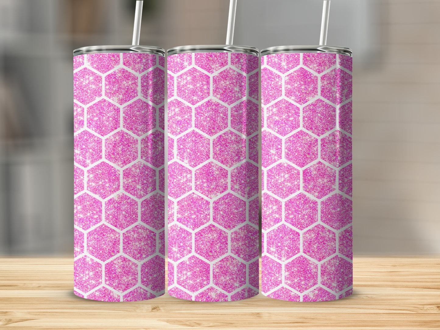 Three glitter pink hexagonal tumblers with white straws on a wood table.