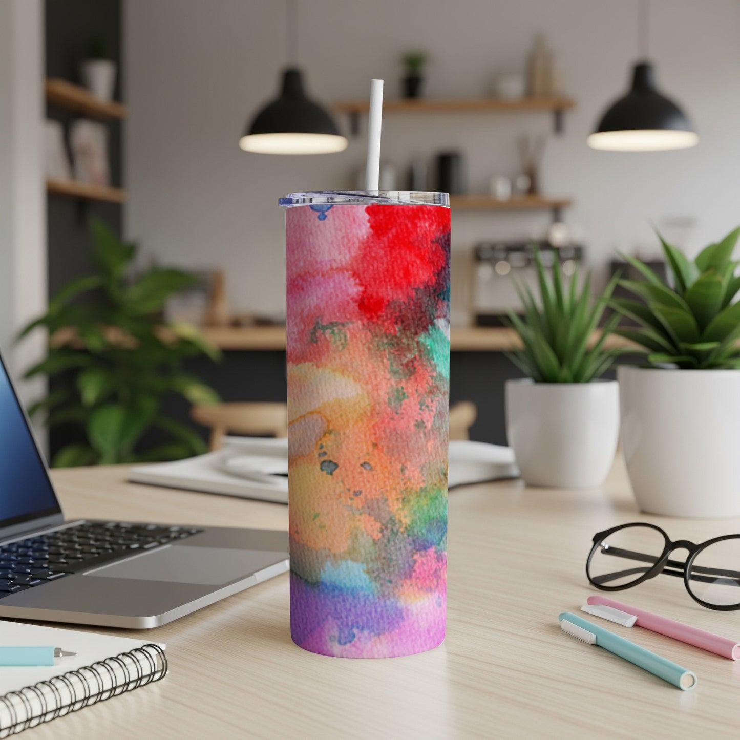 Tumbler with abstract watercolor design and straw on a desk.