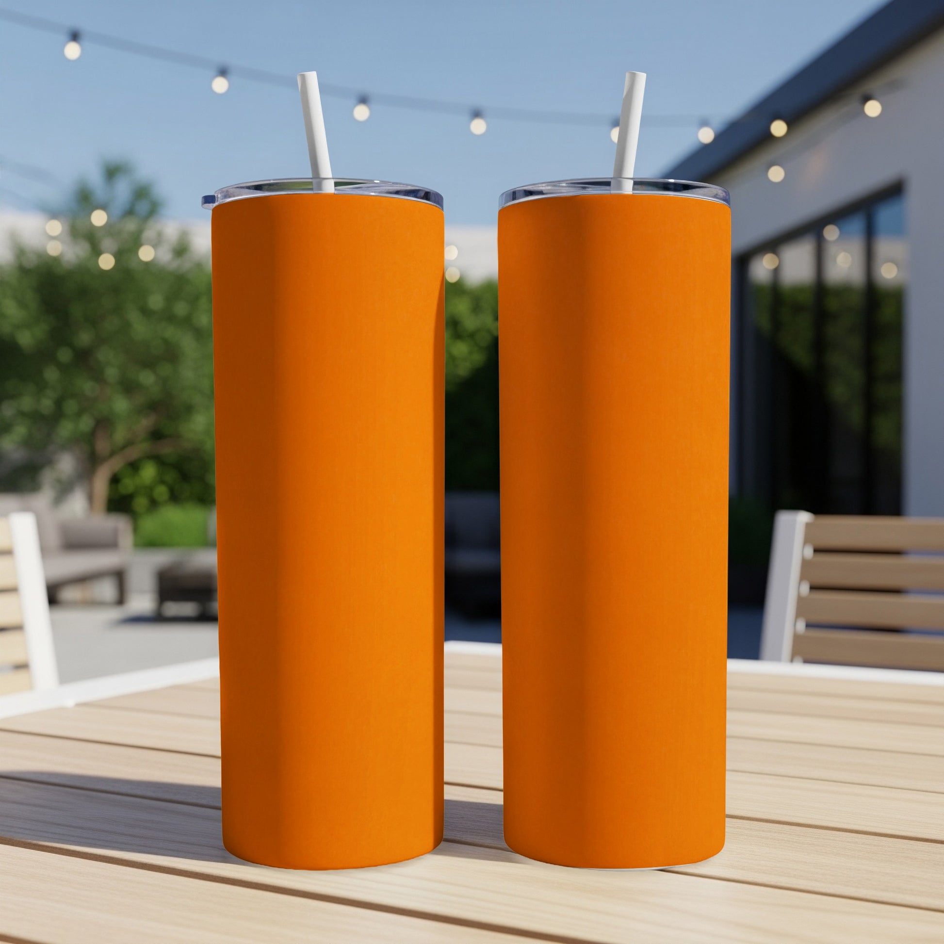 Two tall, orange tumblers with white straws on a wooden table outdoors.