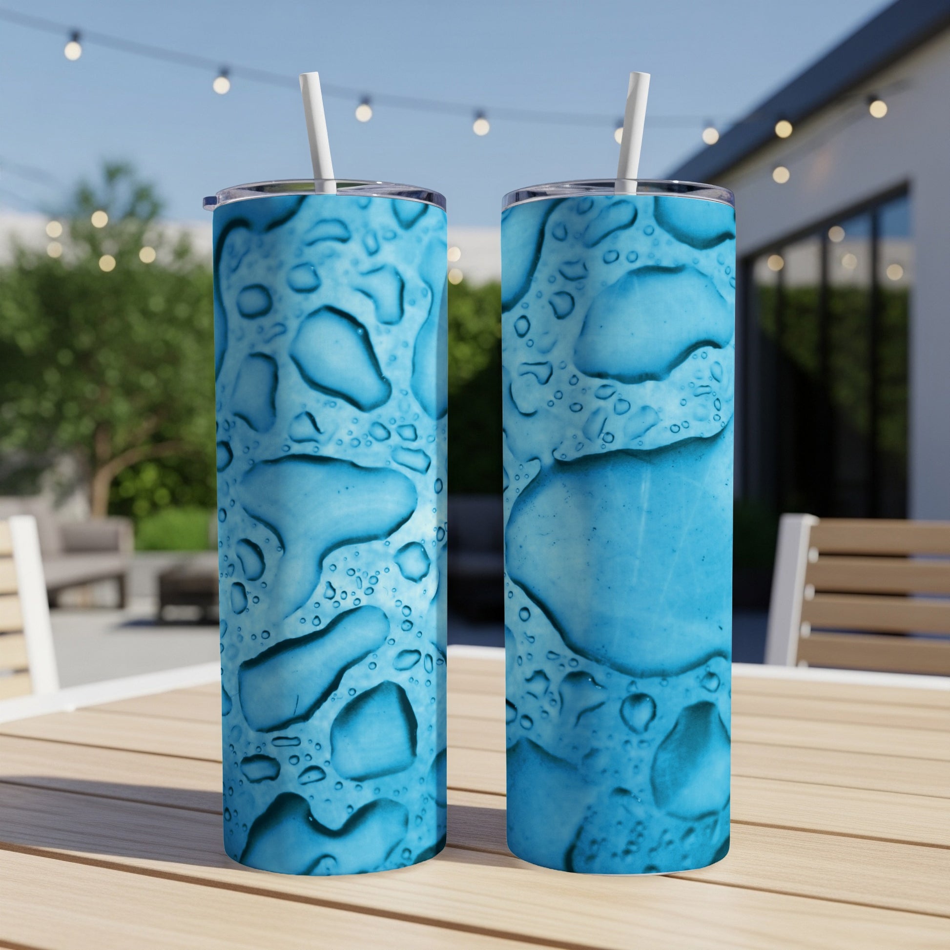 Two blue tumblers with water drop pattern and straws on a wooden table.