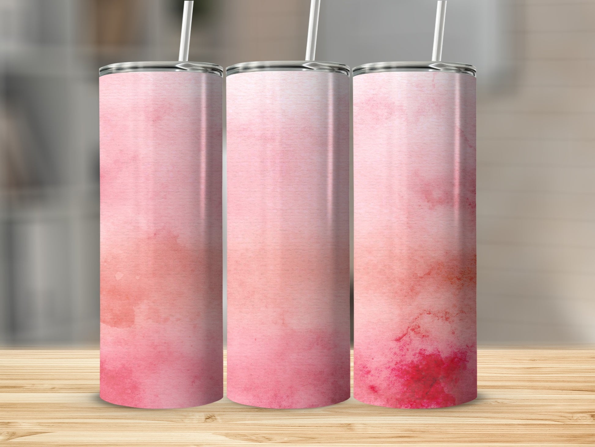 Three pink watercolor tumblers with white straws on a wooden surface.
