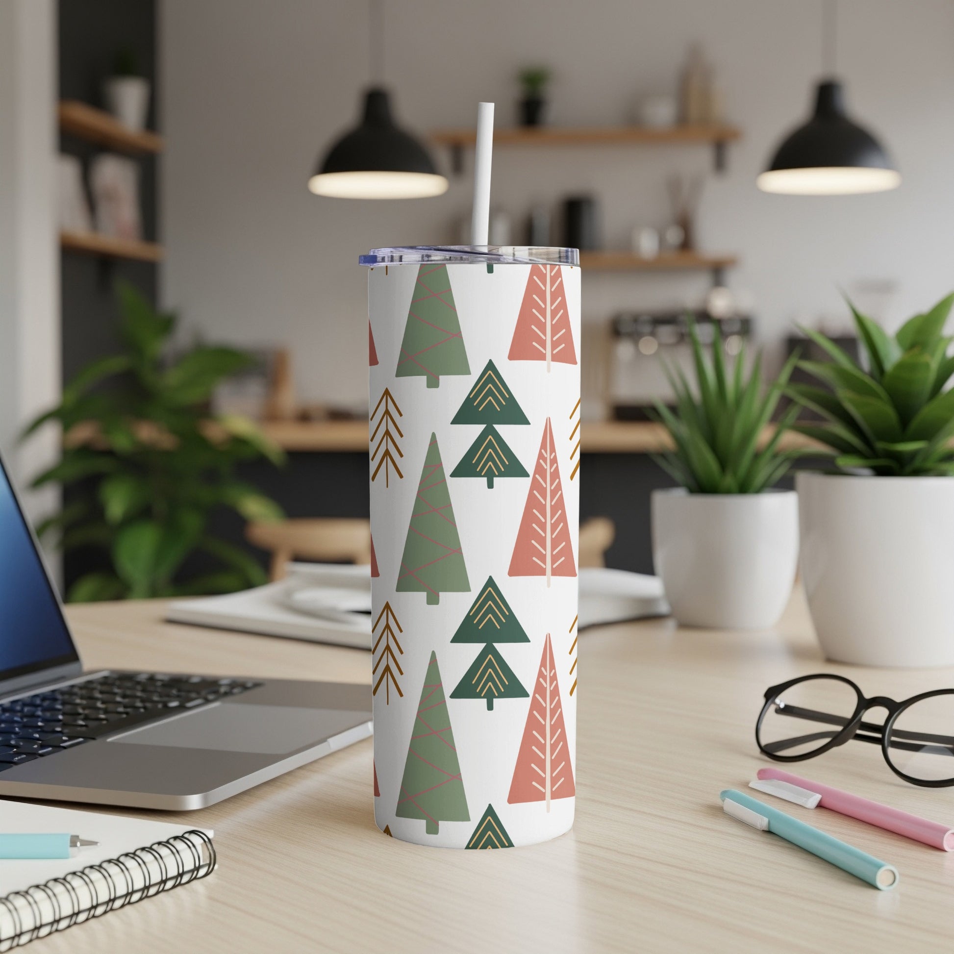 White tumbler with green and pink Christmas tree pattern, on a desk.