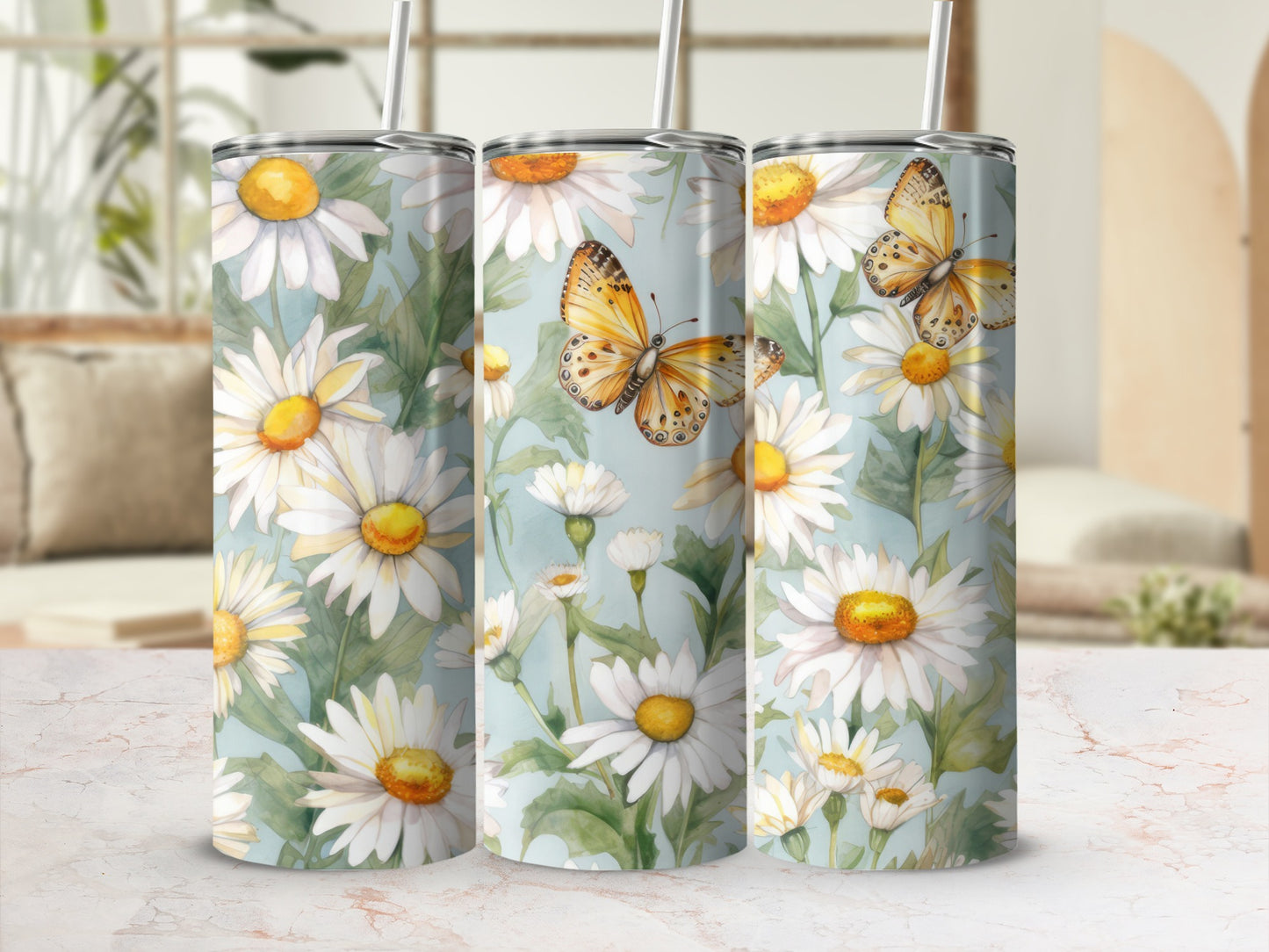 Three tumblers with daisies and butterflies on a countertop.