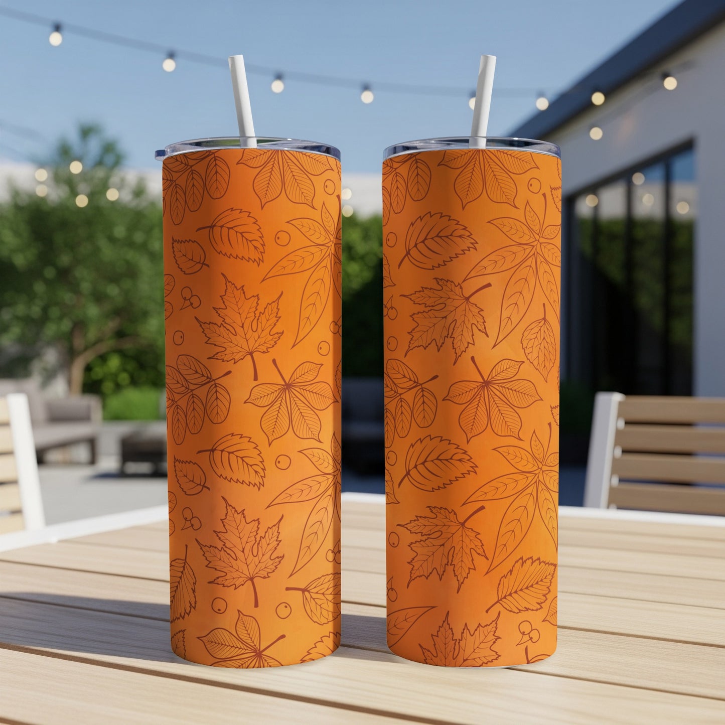 Two orange tumblers with fall leaf pattern on a wooden table.
