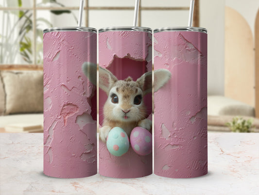 Pink tumbler with a cute bunny peeking through a hole holding Easter eggs.