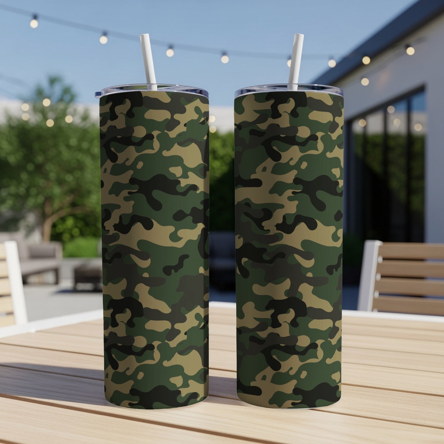 Two camouflage print tumblers with white straws stand on a wooden table outdoors.