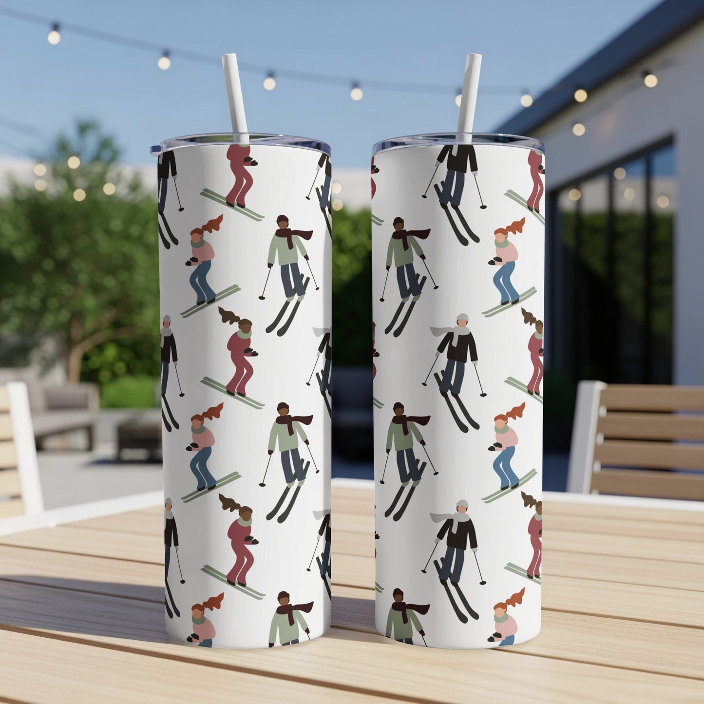 Two white tumblers with repeating pattern of skiers on a table outdoors.