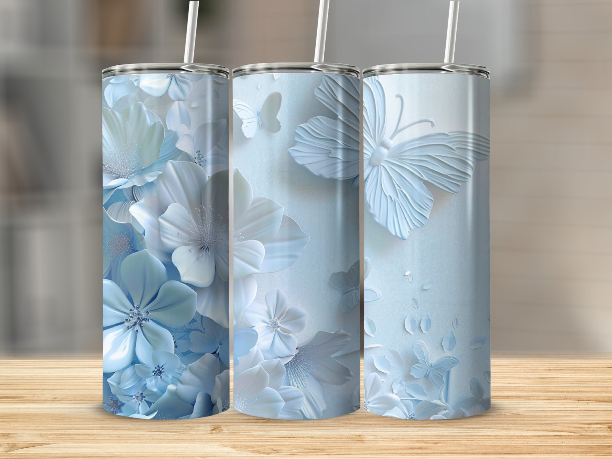 Three blue floral and butterfly tumblers with straws on a wooden surface.