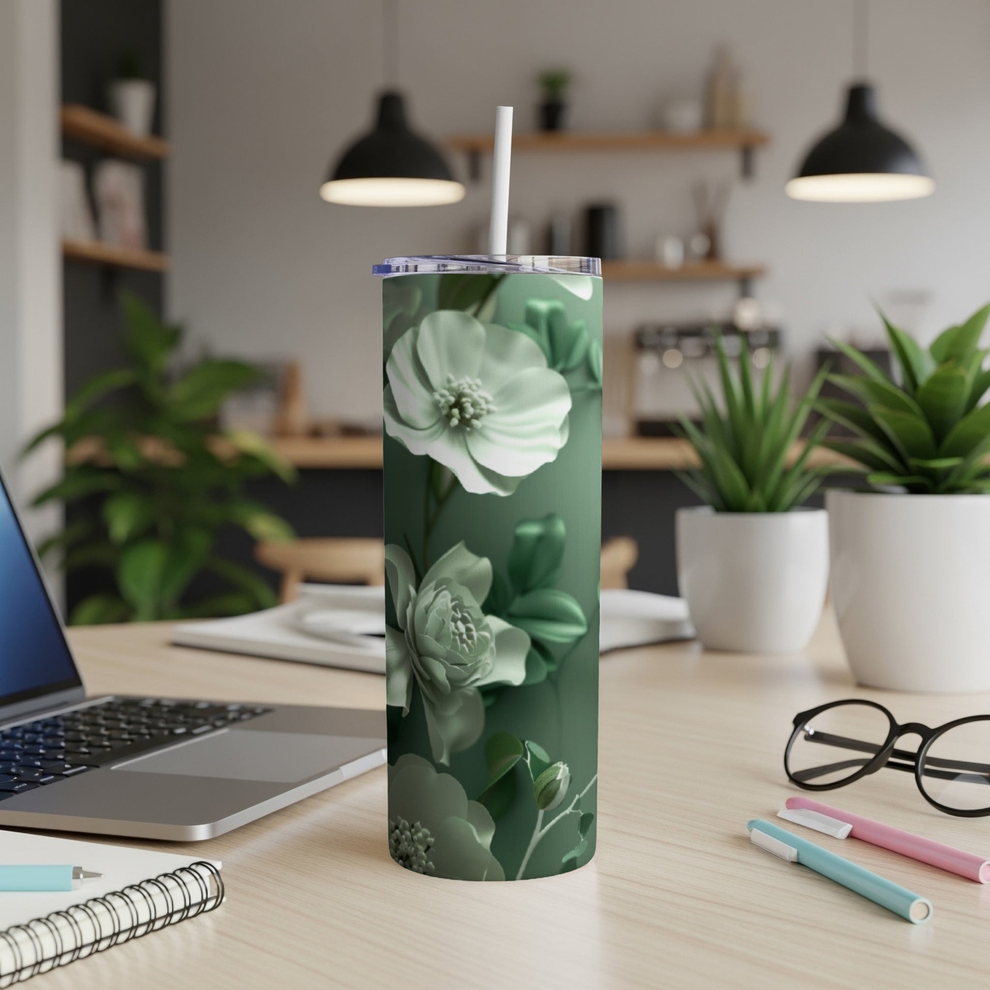 Green floral tumbler with straw on desk next to laptop and pens.